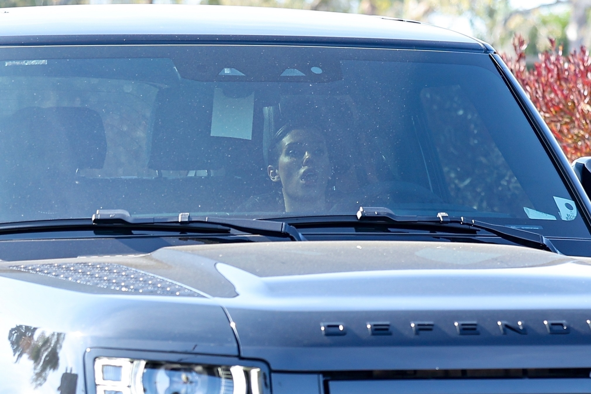 A person with short hair is visible through the windshield of a gray SUV