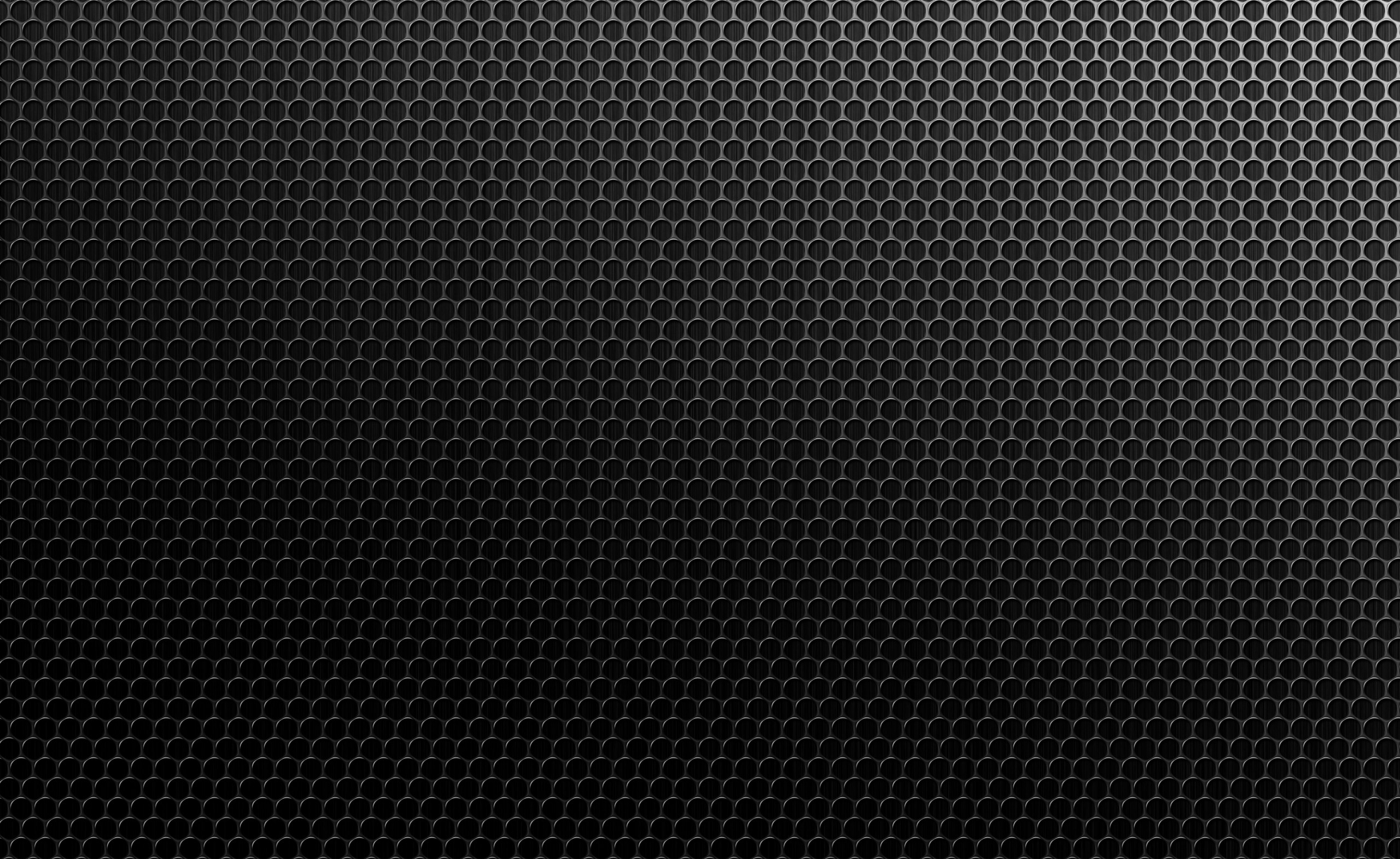 Dark and textured background of a black metal grill with circular holes, creating a cool and modern wallpaper