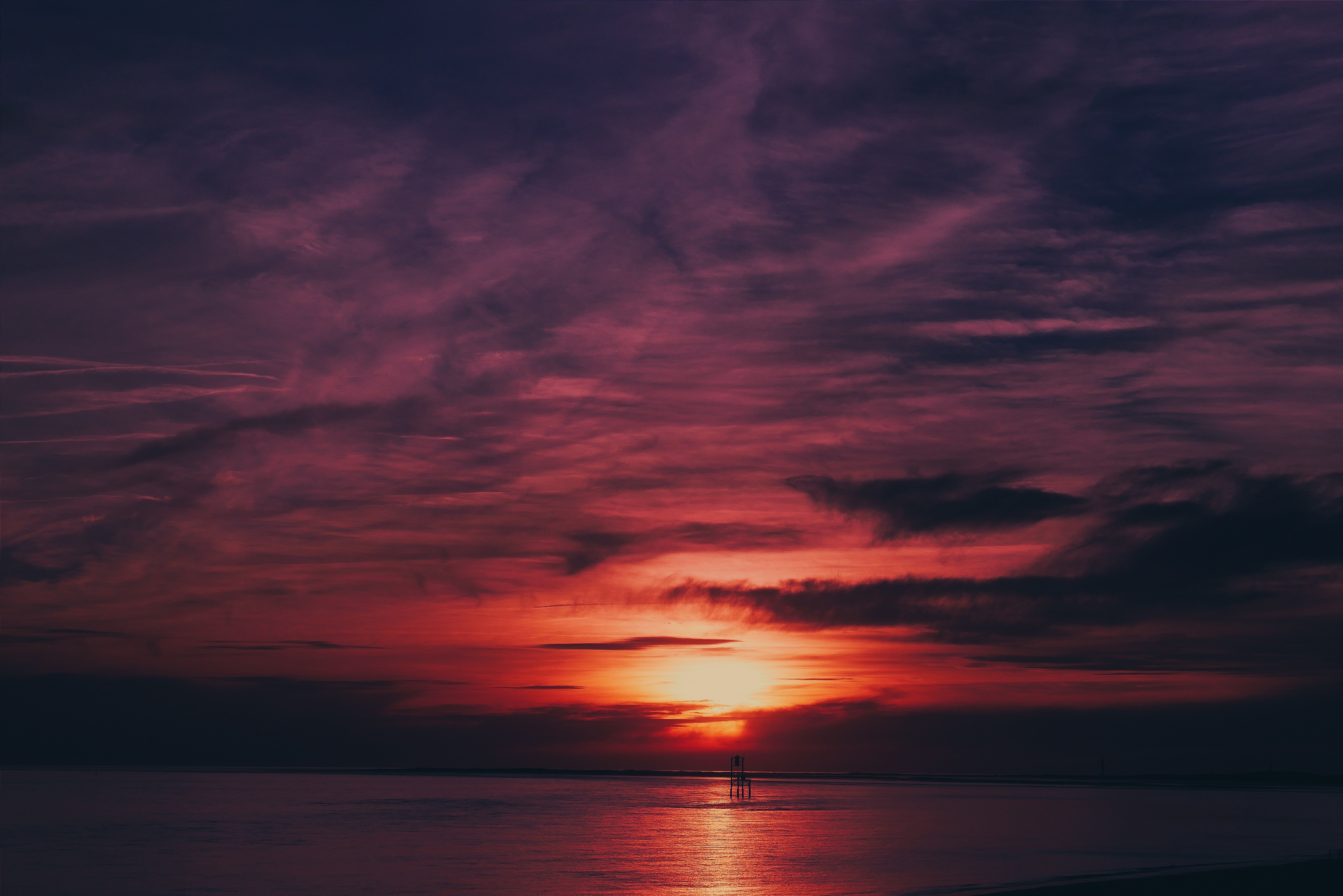 A breathtaking sunset over a tranquil body of water, with vibrant hues of red, orange, and purple painting the sky and reflecting on the water's surface