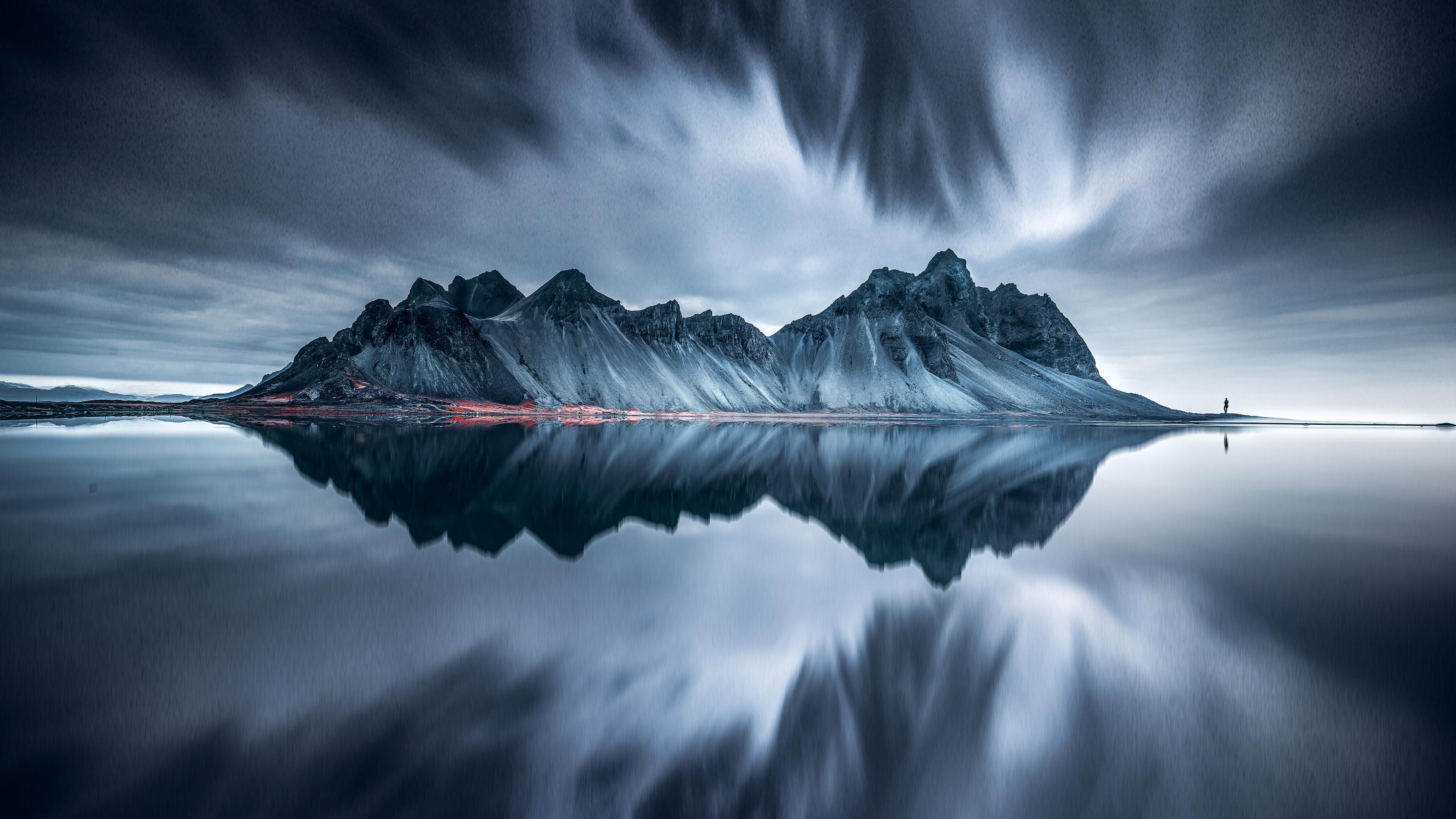 A breathtaking 8K HD wallpaper showcasing a dramatic mountain range reflected in a serene lake, under a moody sky