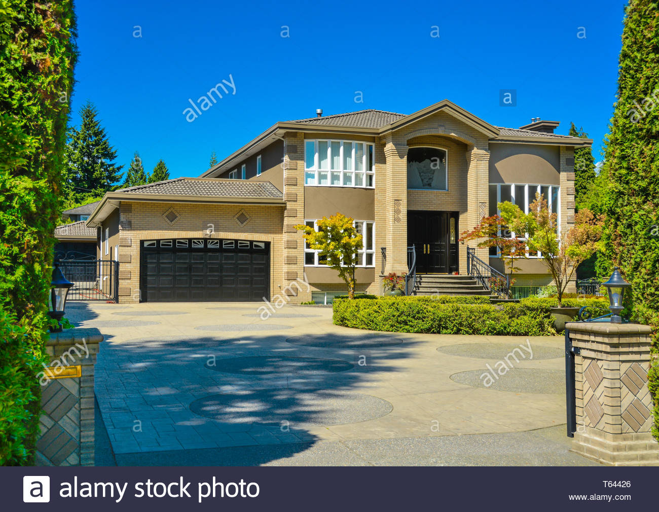 Front Yard Of Luxury Family House With Paved Driveway On Blue Sky