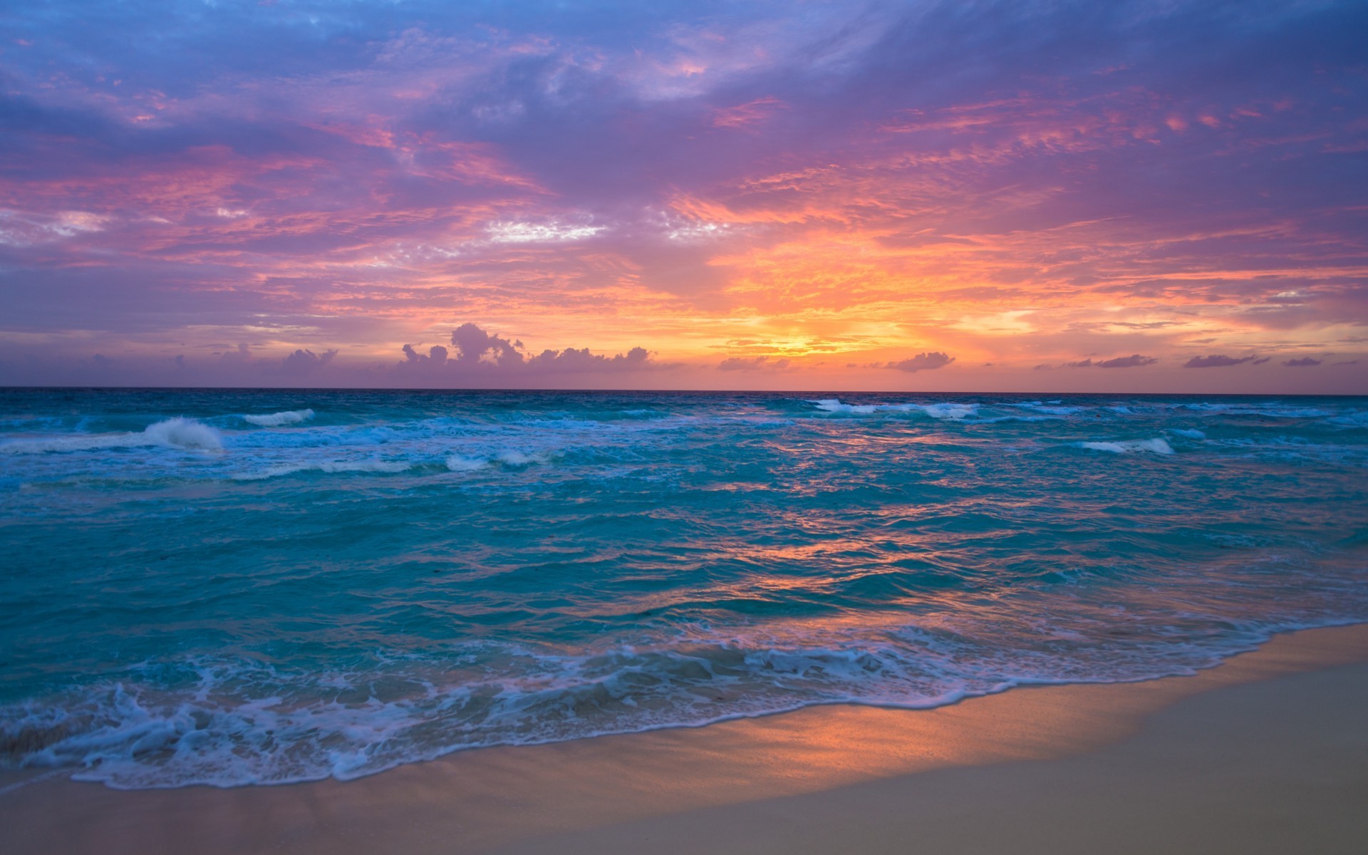 Vivid sunset over a tranquil turquoise ocean, casting a warm glow on the sandy beach