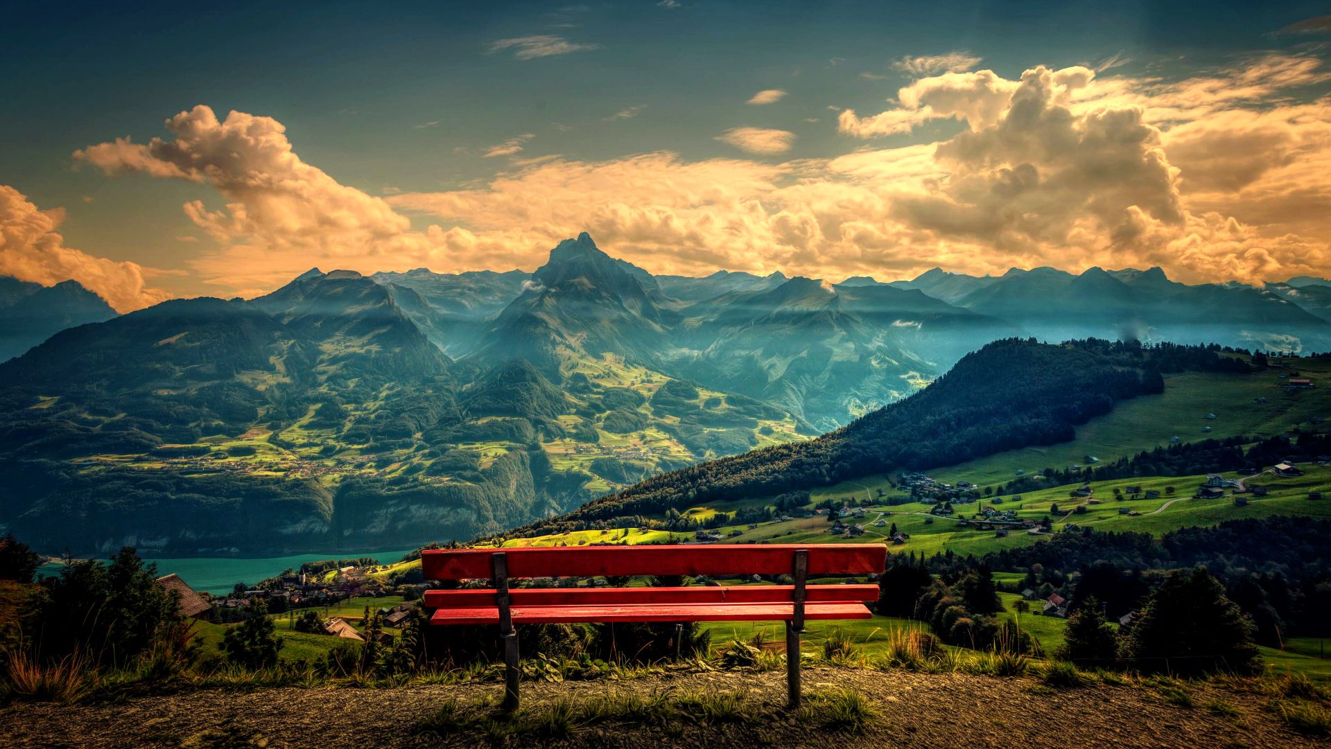 A breathtaking 4K scenery wallpaper featuring a vibrant red bench overlooking a stunning valley landscape with majestic mountains, a tranquil lake, and lush greenery under a picturesque sky