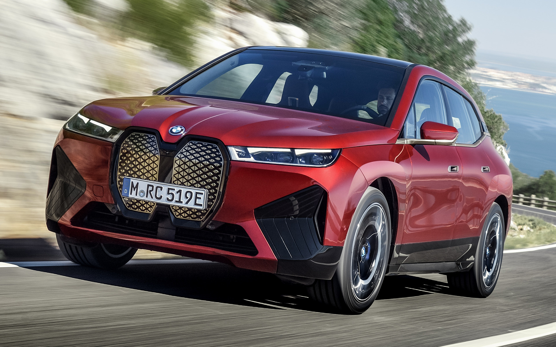 Red BMW iX electric SUV driving on a coastal road