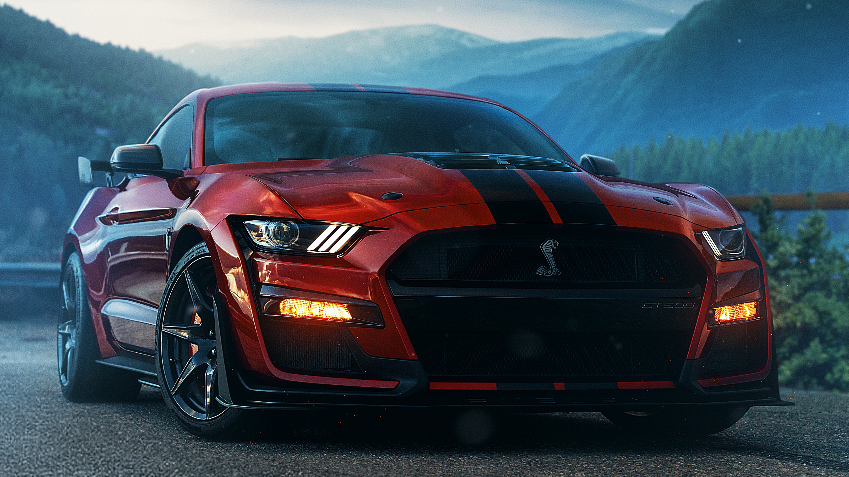 A vibrant red Ford Mustang Shelby GT500 parked on a mountain road, with its iconic cobra emblem displayed prominently. The backdrop showcases a stunning mountainous landscape with lush greenery and a misty atmosphere