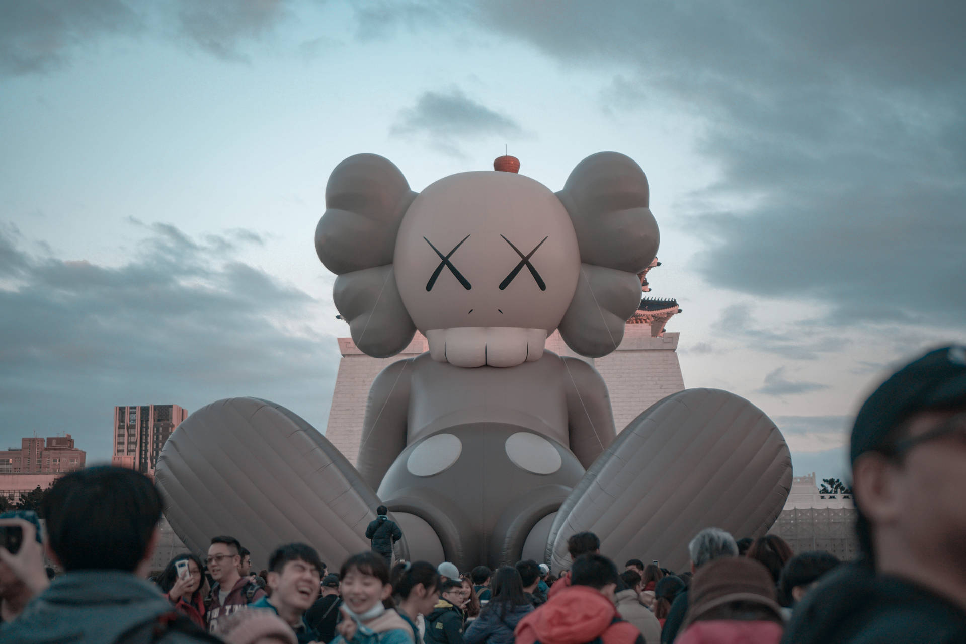A giant inflatable KAWS Companion figure sits in front of a crowd of people