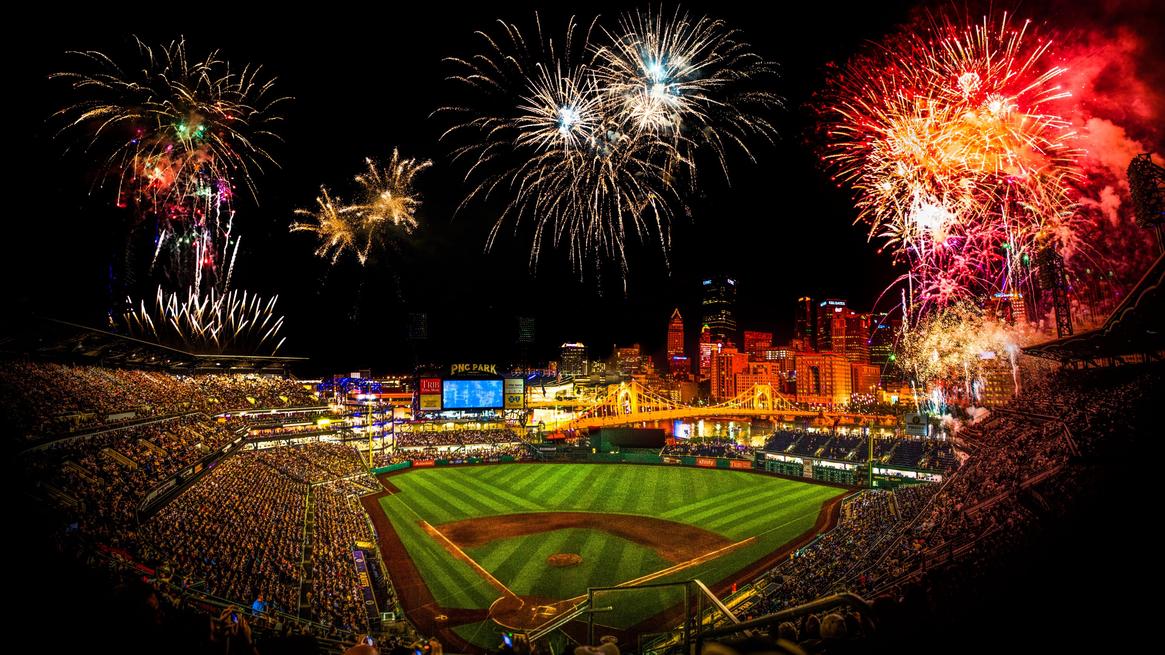 Fireworks light up the night sky over a packed baseball stadium, creating a vibrant and celebratory atmosphere