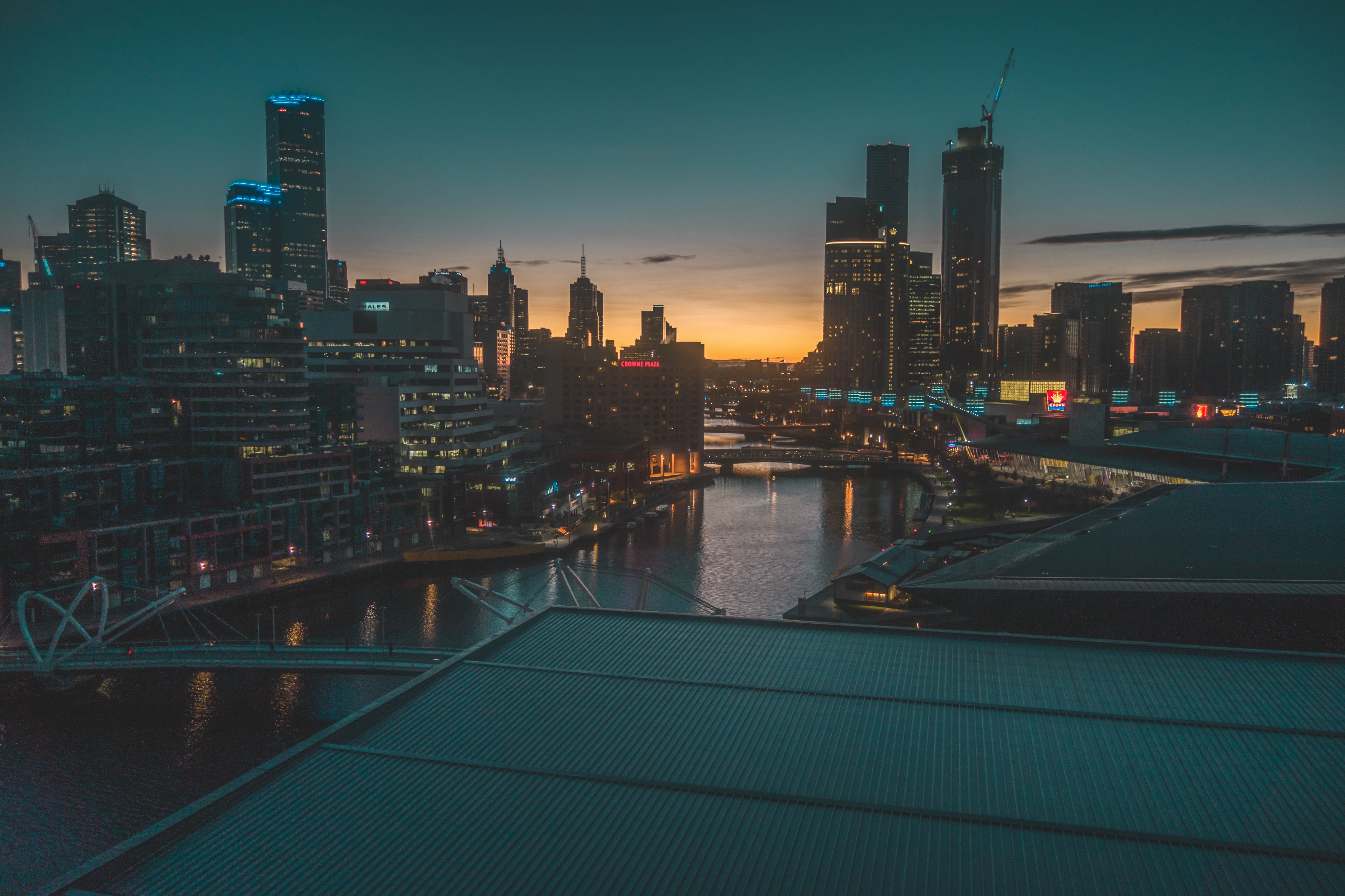 5K HD wallpaper of a cityscape at dusk, featuring a river, modern buildings, and a vibrant sunset