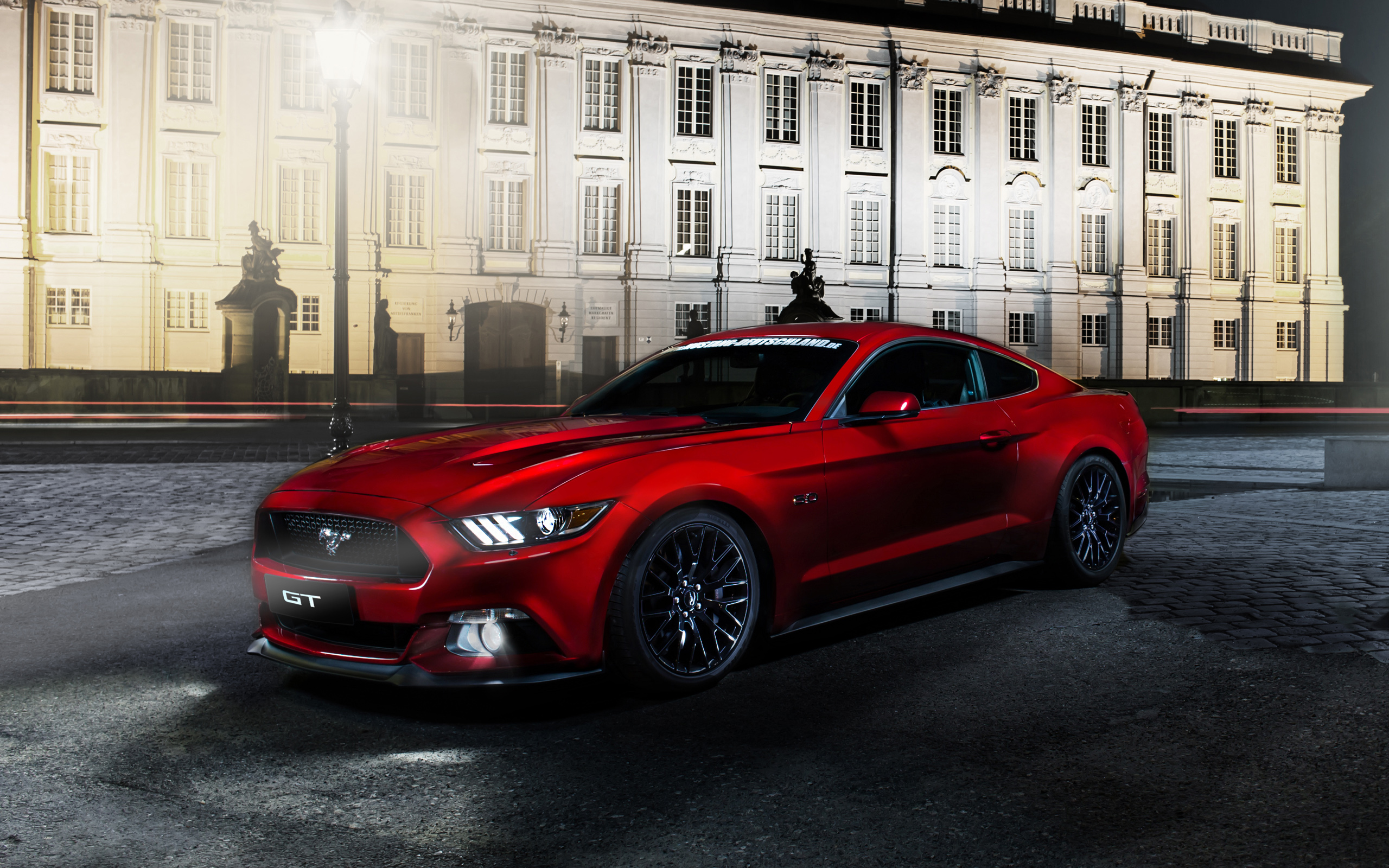 Red Ford Mustang GT parked in front of a grand building at night