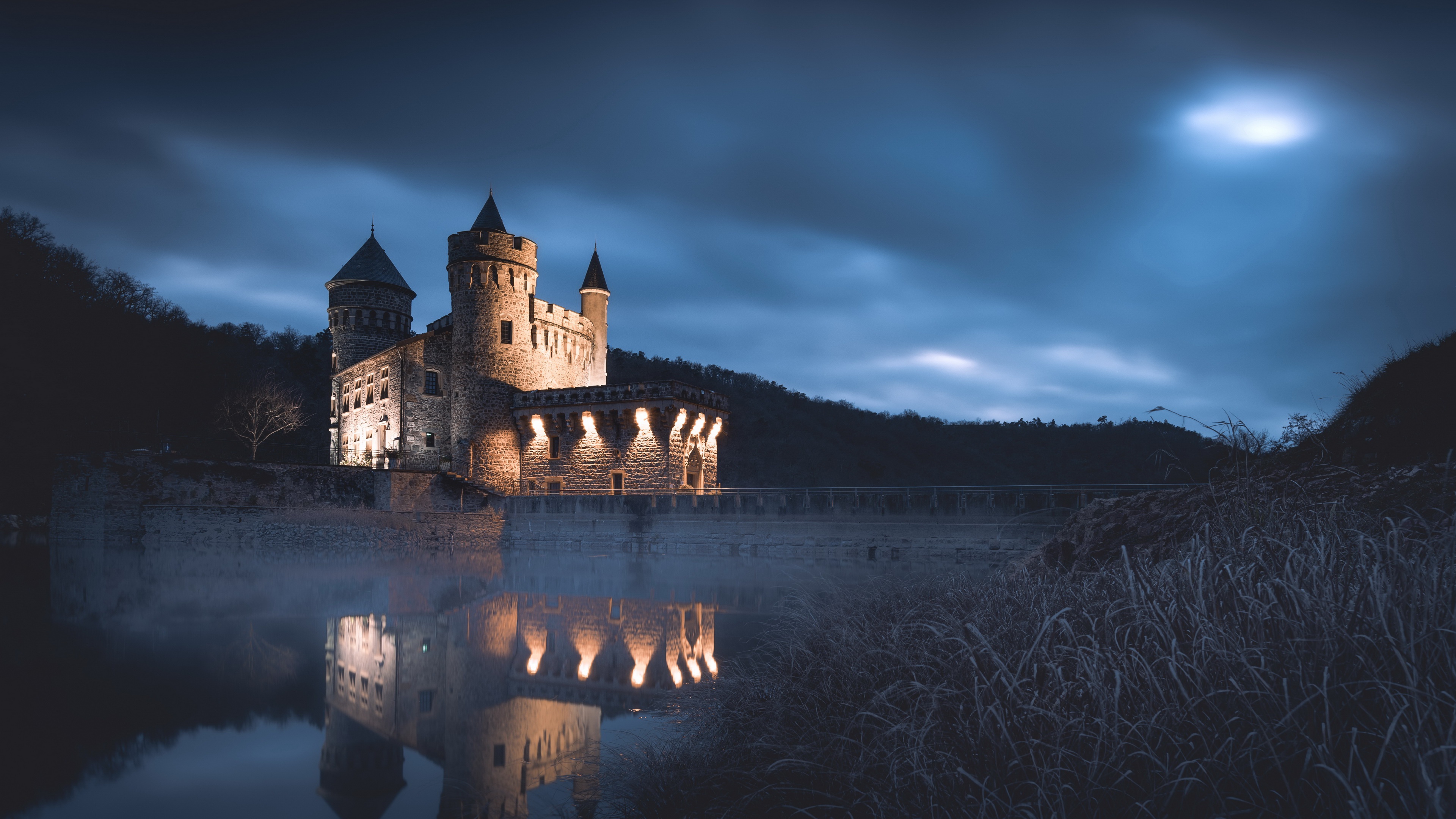 A majestic castle illuminated at night, reflected in the still water below, with a misty, ethereal atmosphere