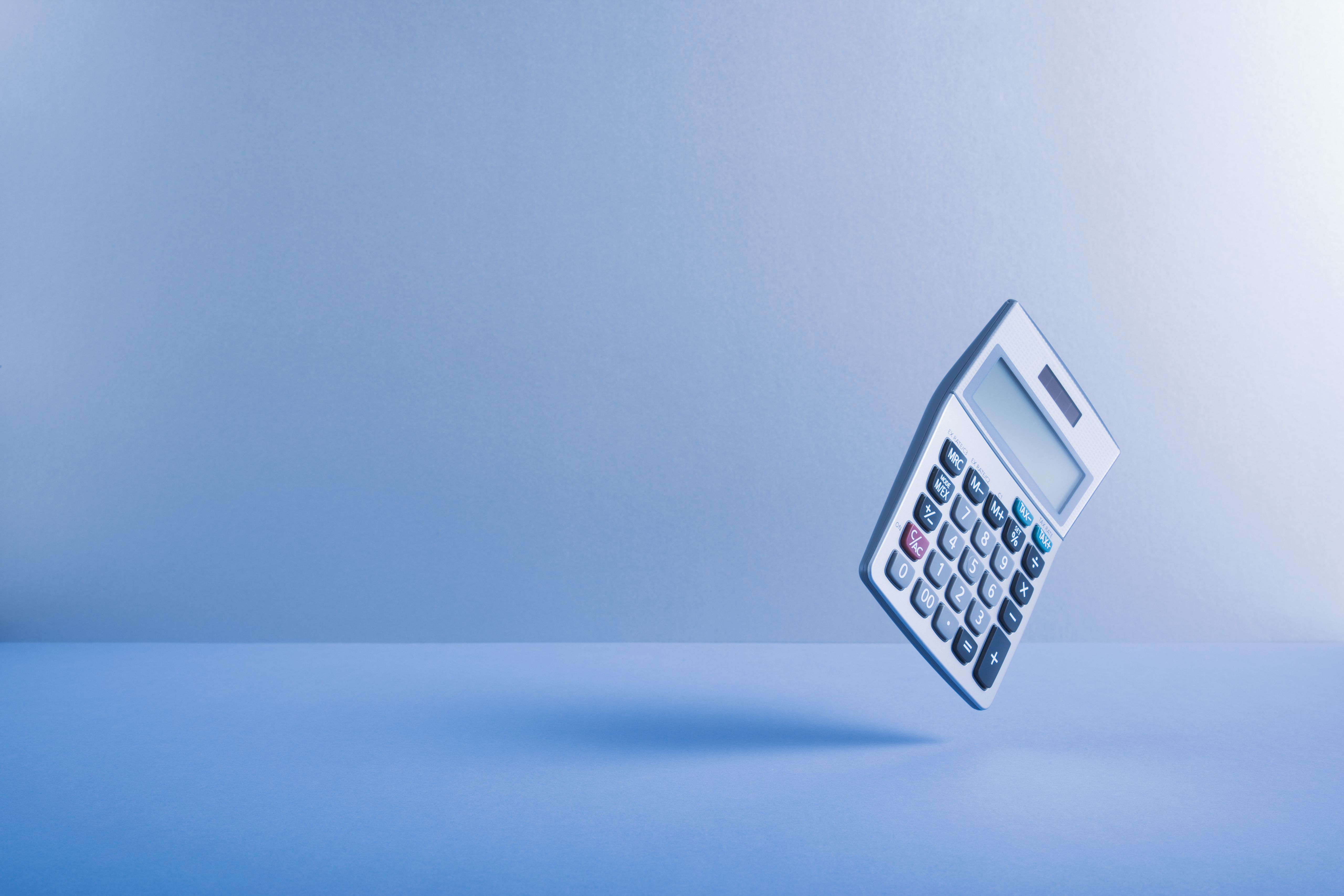 A calculator hovers in a minimalist blue studio setting, evoking concepts of finance, accounting, and business calculations