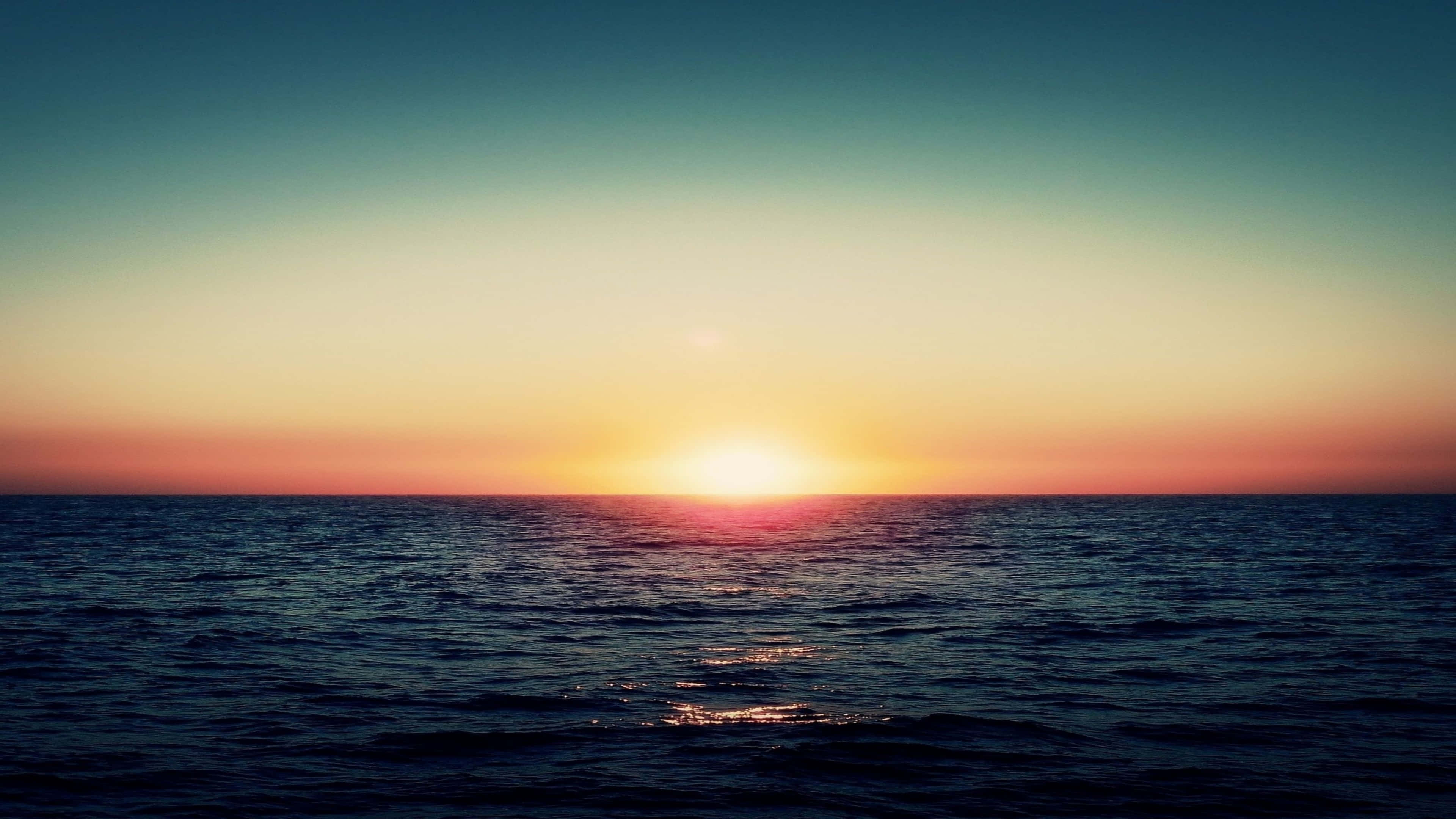 Sunset over a calm ocean, with the sun low on the horizon and a gradient of colors in the sky