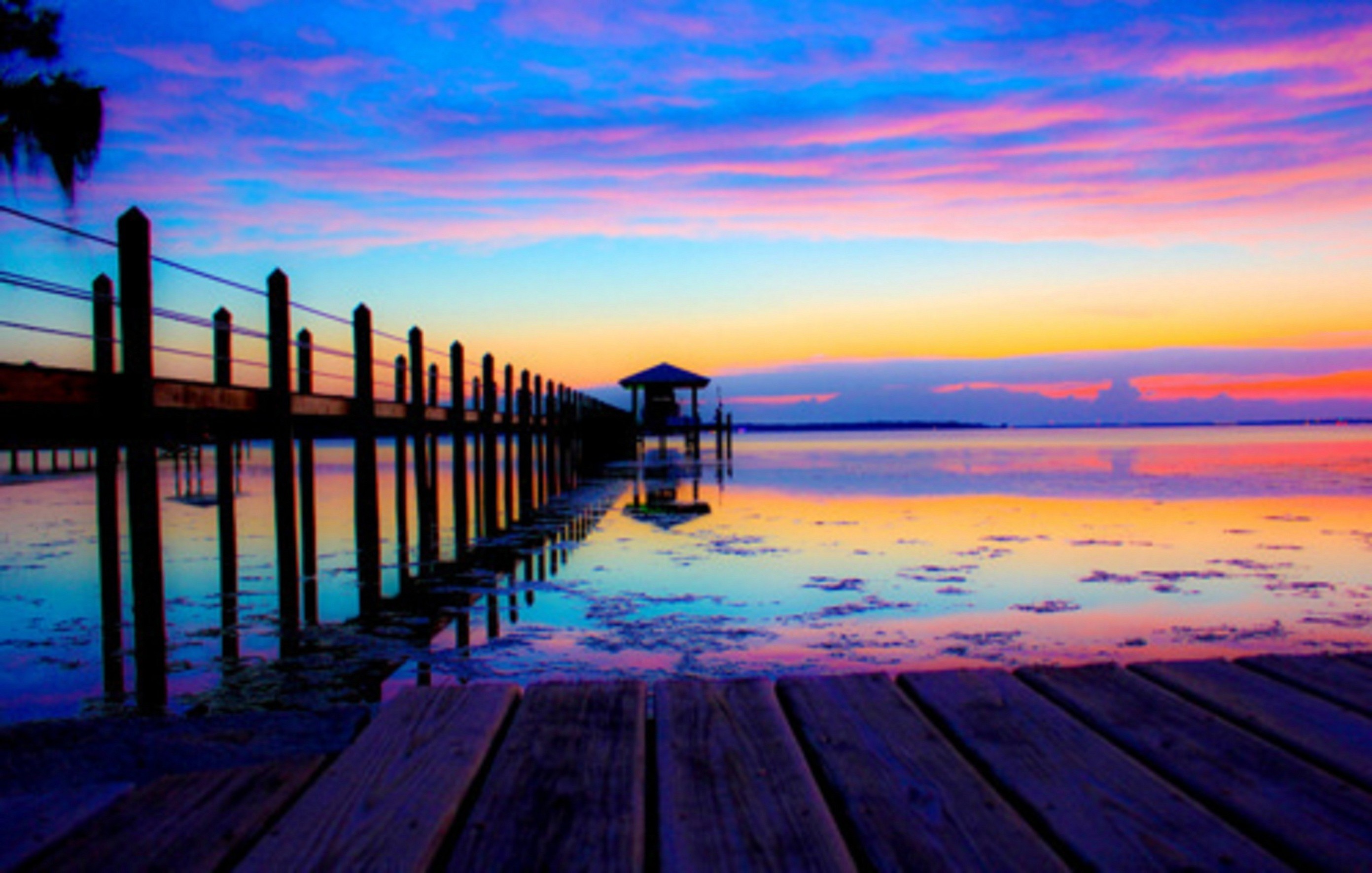 A vibrant sunset over a tranquil beach with a wooden pier stretching into the colorful water