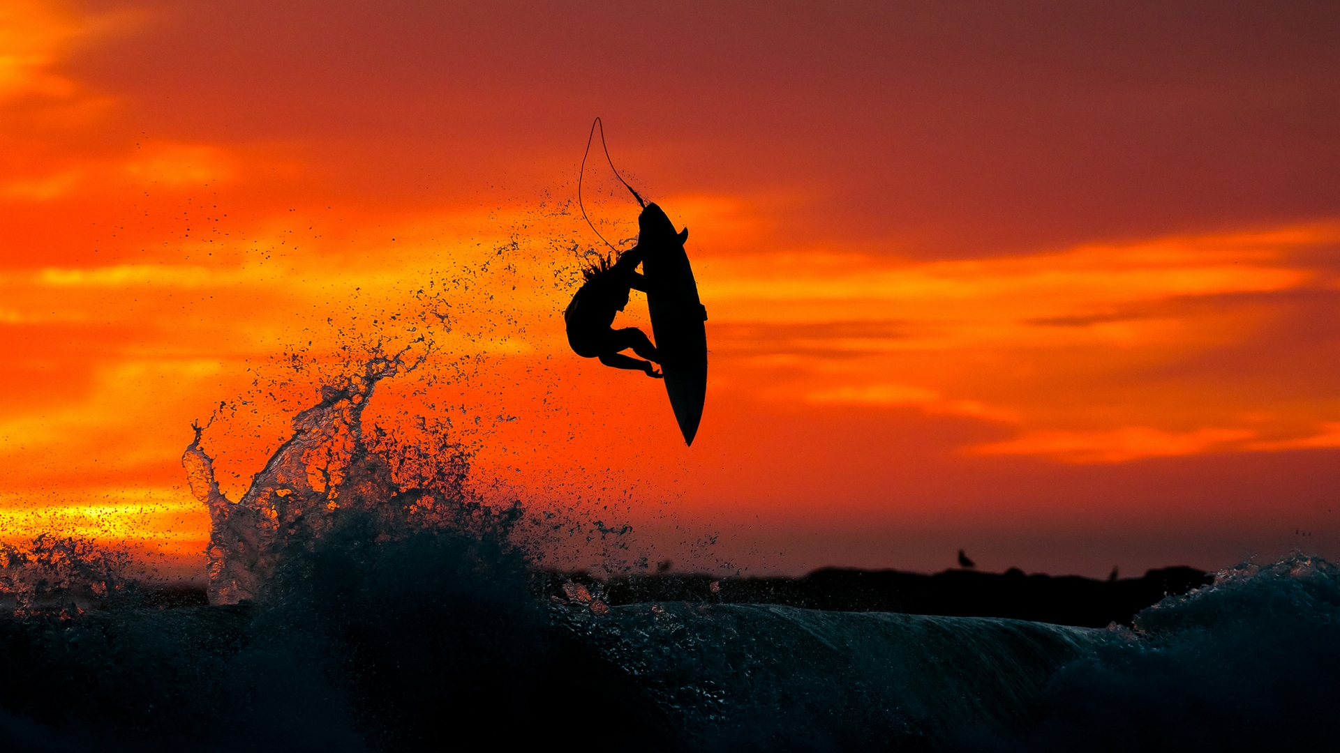 Silhouette of a surfer performing an aerial maneuver against a vibrant sunset backdrop