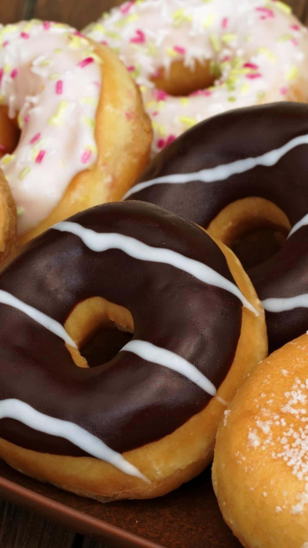 A Plate Of Donuts With Frosting And Sprinkles Wallpaper