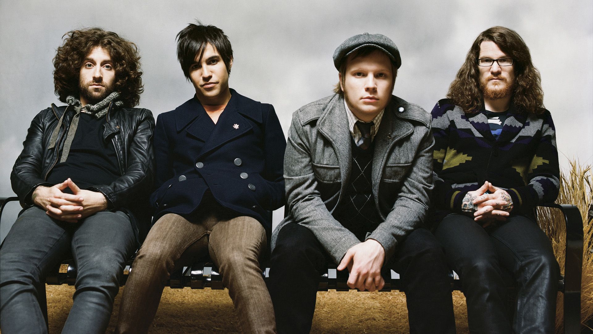 The members of Fall Out Boy sit on a bench, posing for a photo