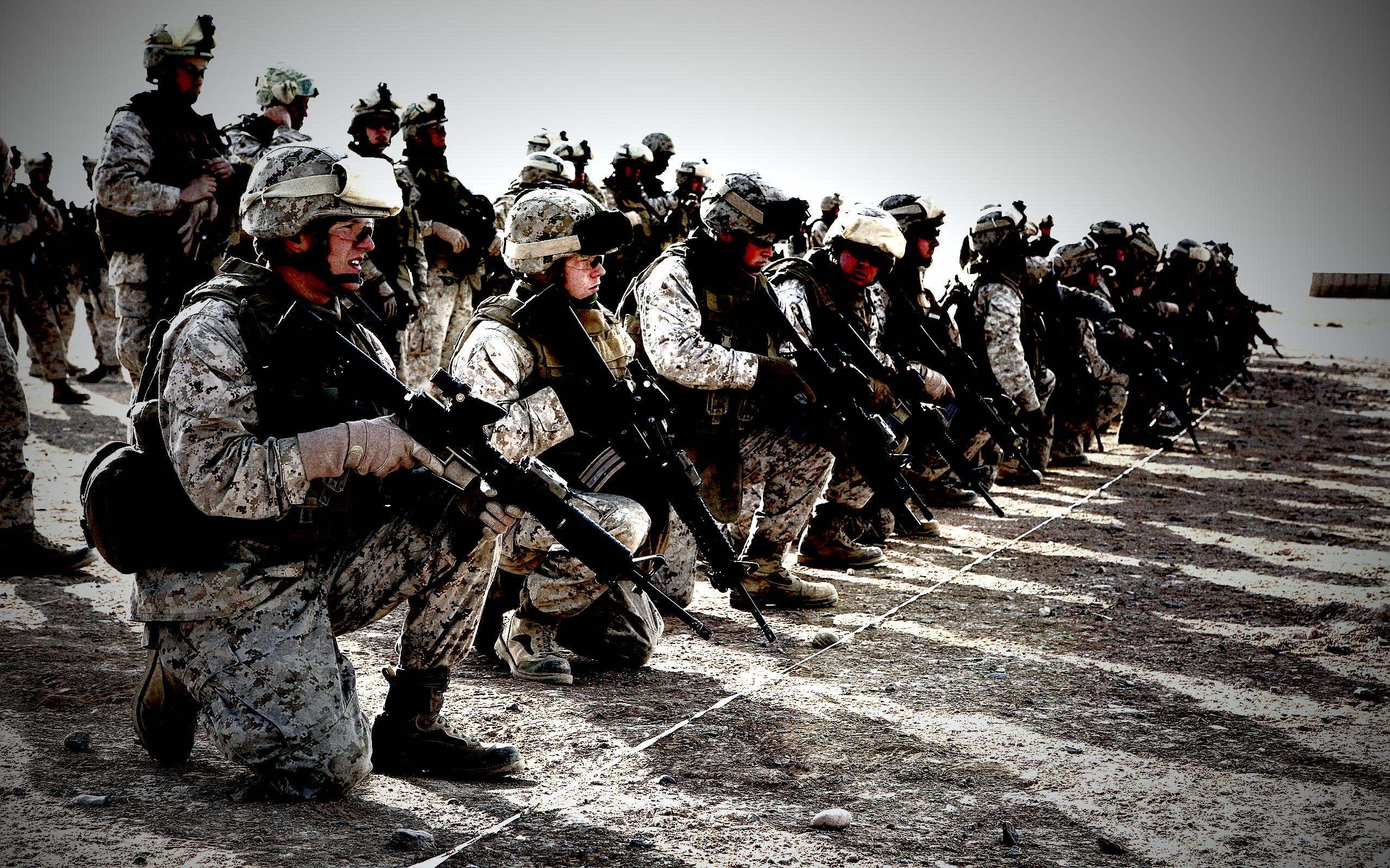 A line of kneeling soldiers in camouflage uniforms, holding rifles, against a stark desert backdrop