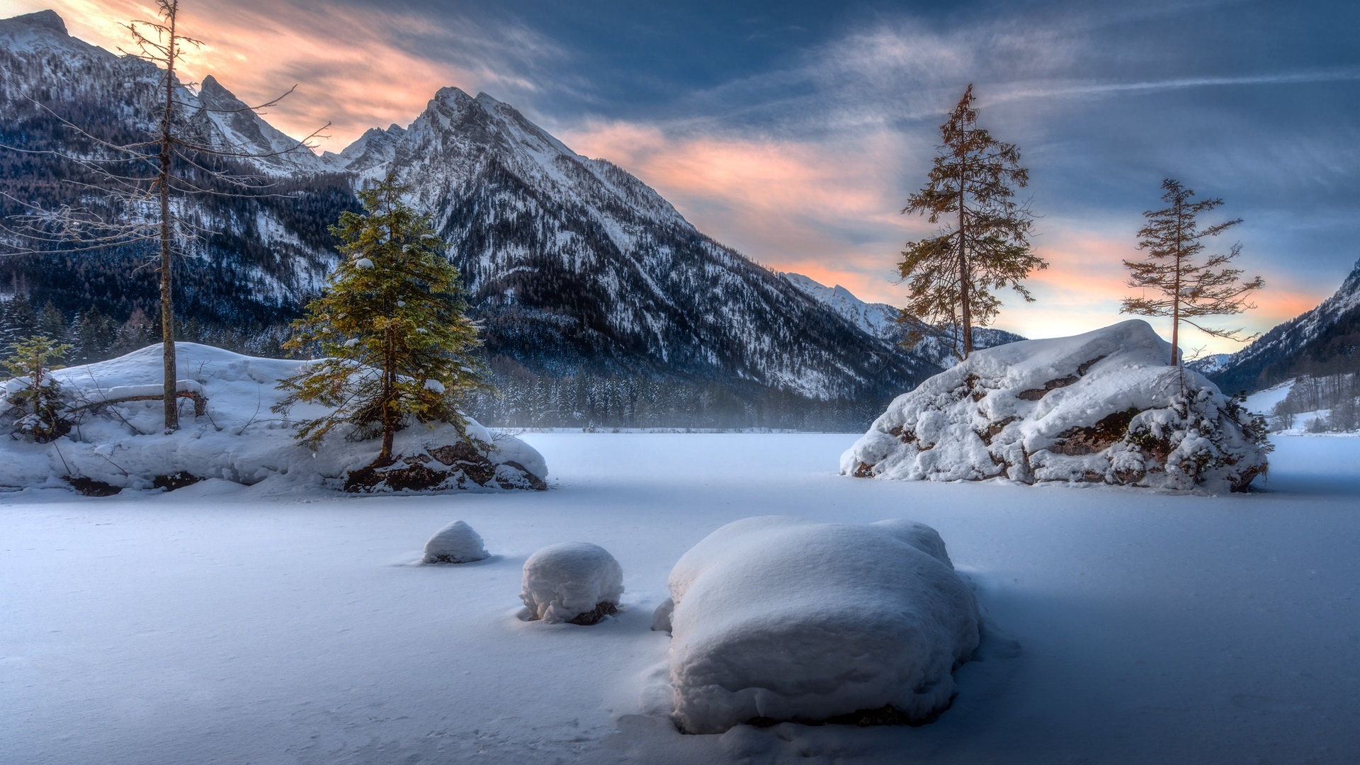 A breathtaking winter landscape with snow-covered mountains, frozen lake, and evergreen trees at sunset