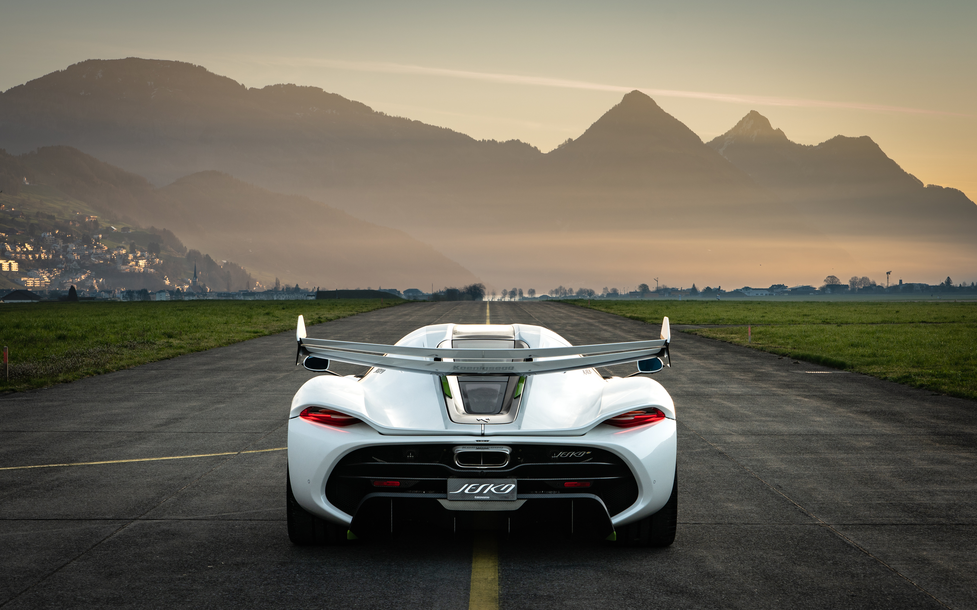 Rear view of a white Koenigsegg Jesko parked on an airstrip with mountains in the background