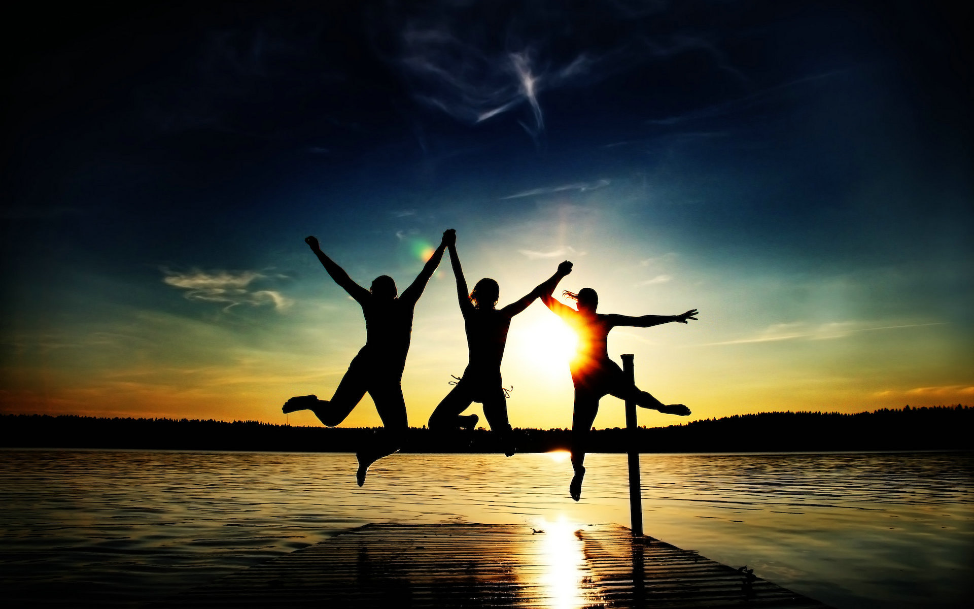 Silhouettes of three friends jumping joyfully on a dock at sunset, celebrating their friendship