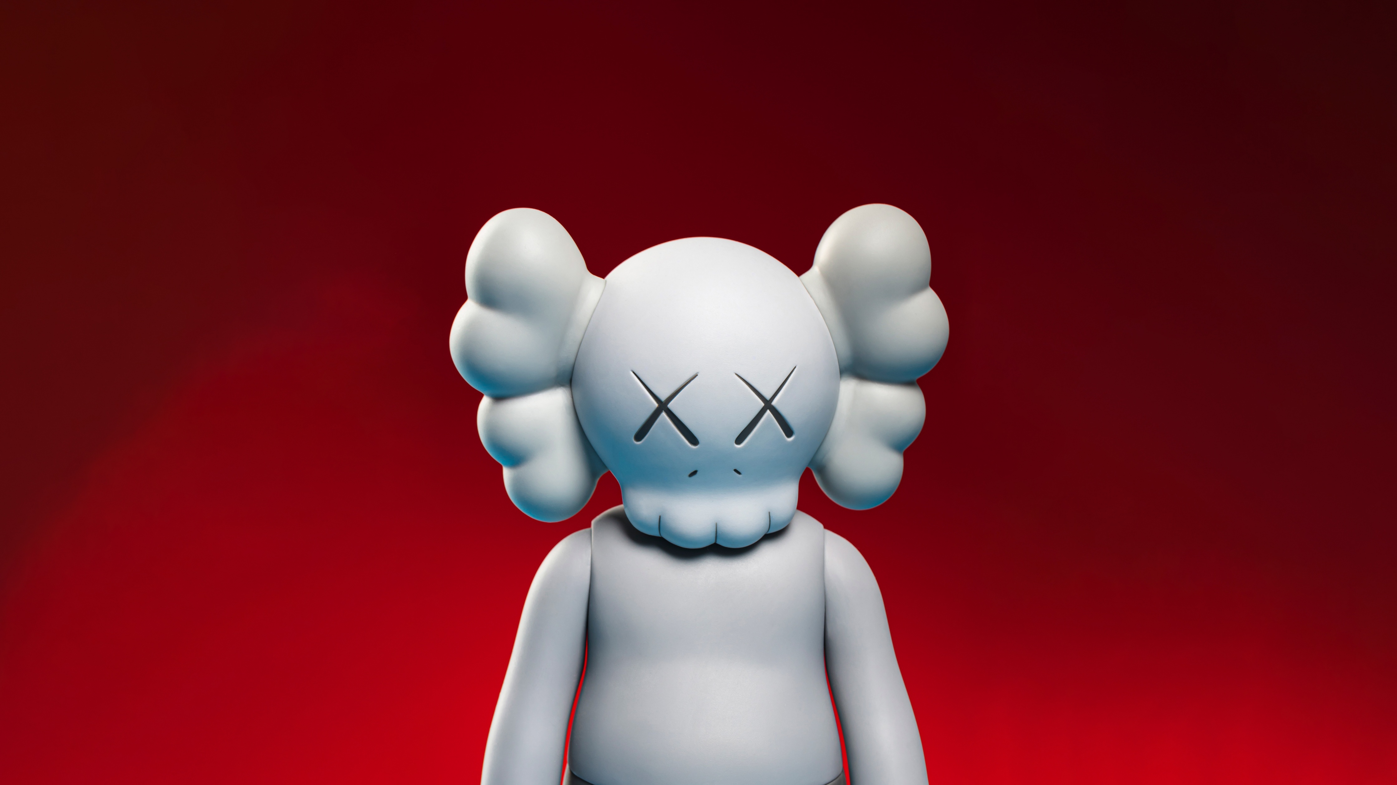 A close-up of a Kaws Companion figure against a vibrant red background, highlighting its iconic X-ed out eyes and minimalist design