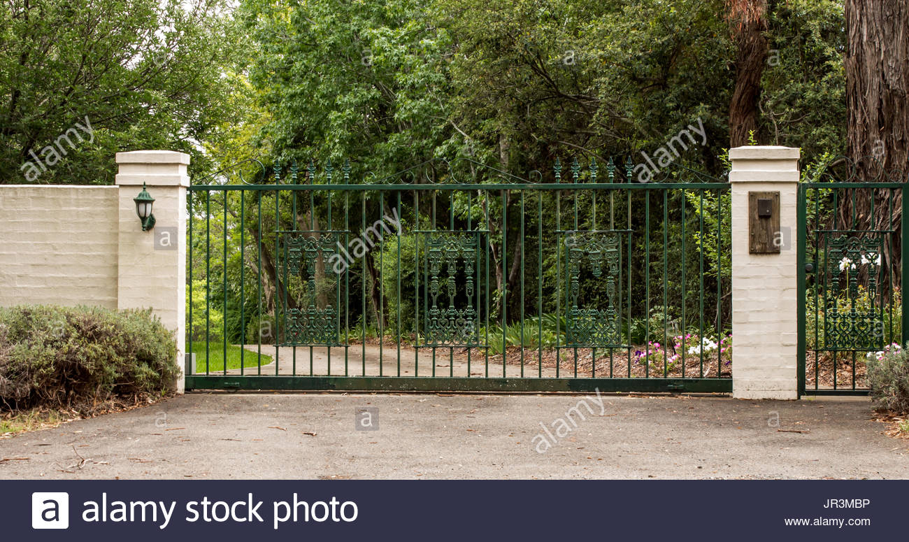 Metal Driveway Entrance Gates Set In Brick Fence With Garden Trees