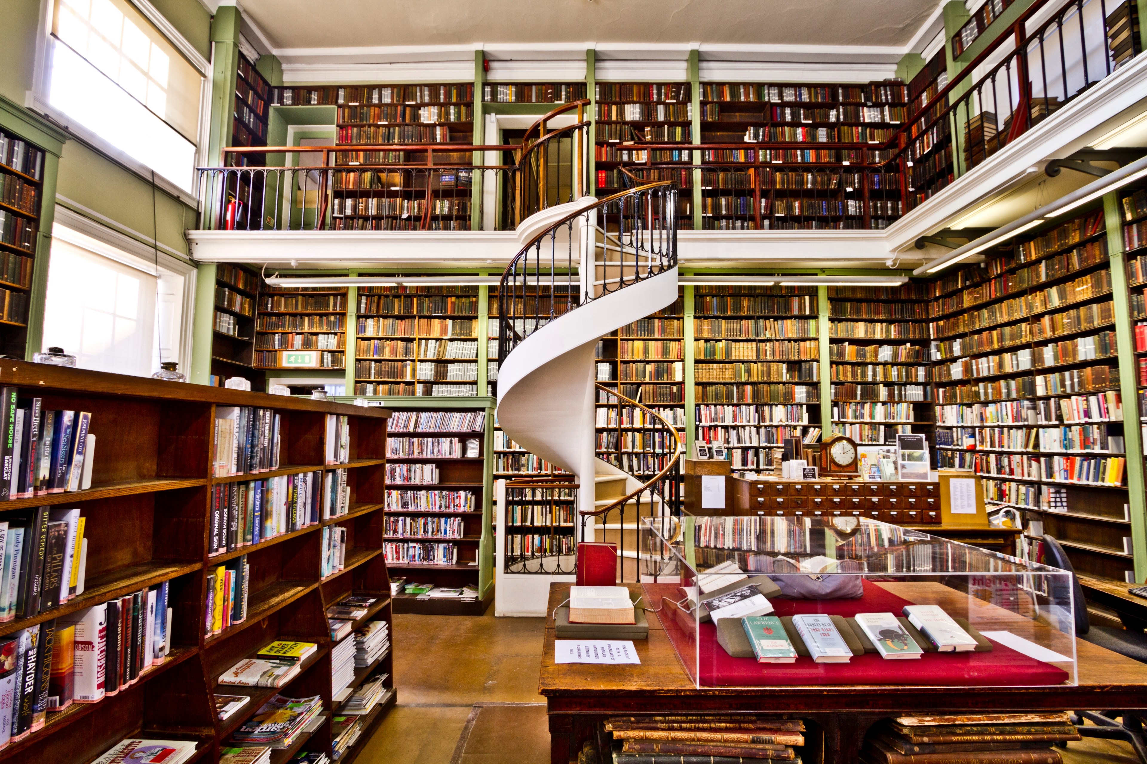 A stunning 4K wallpaper of a multi-level library with a spiral staircase, filled with bookshelves and warm lighting