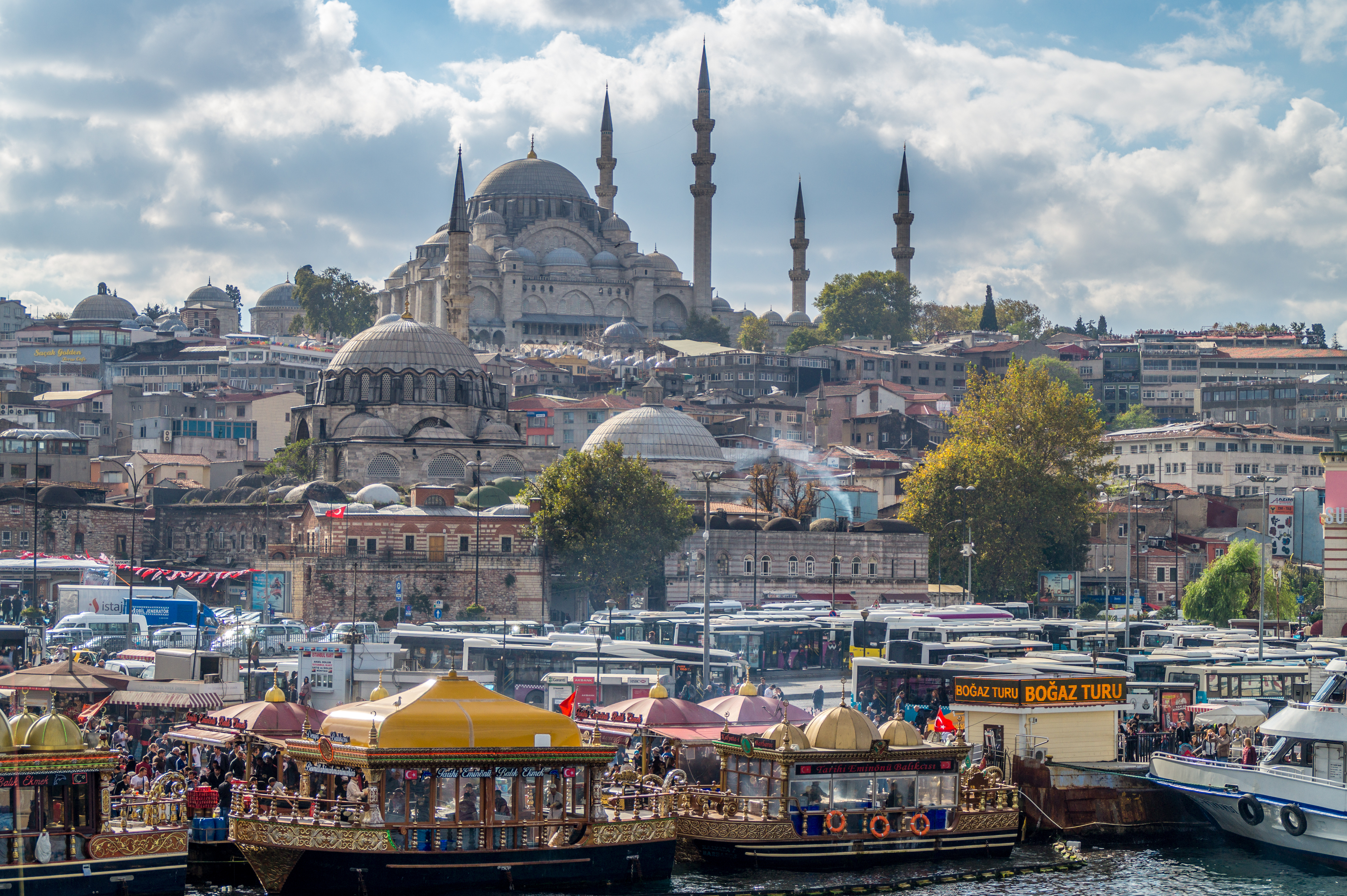 View of Süleymaniye Mosque from the Golden Horn in Istanbul, Turkey. Colorful boats and ferries line the waterfront with the mosque and cityscape in the background