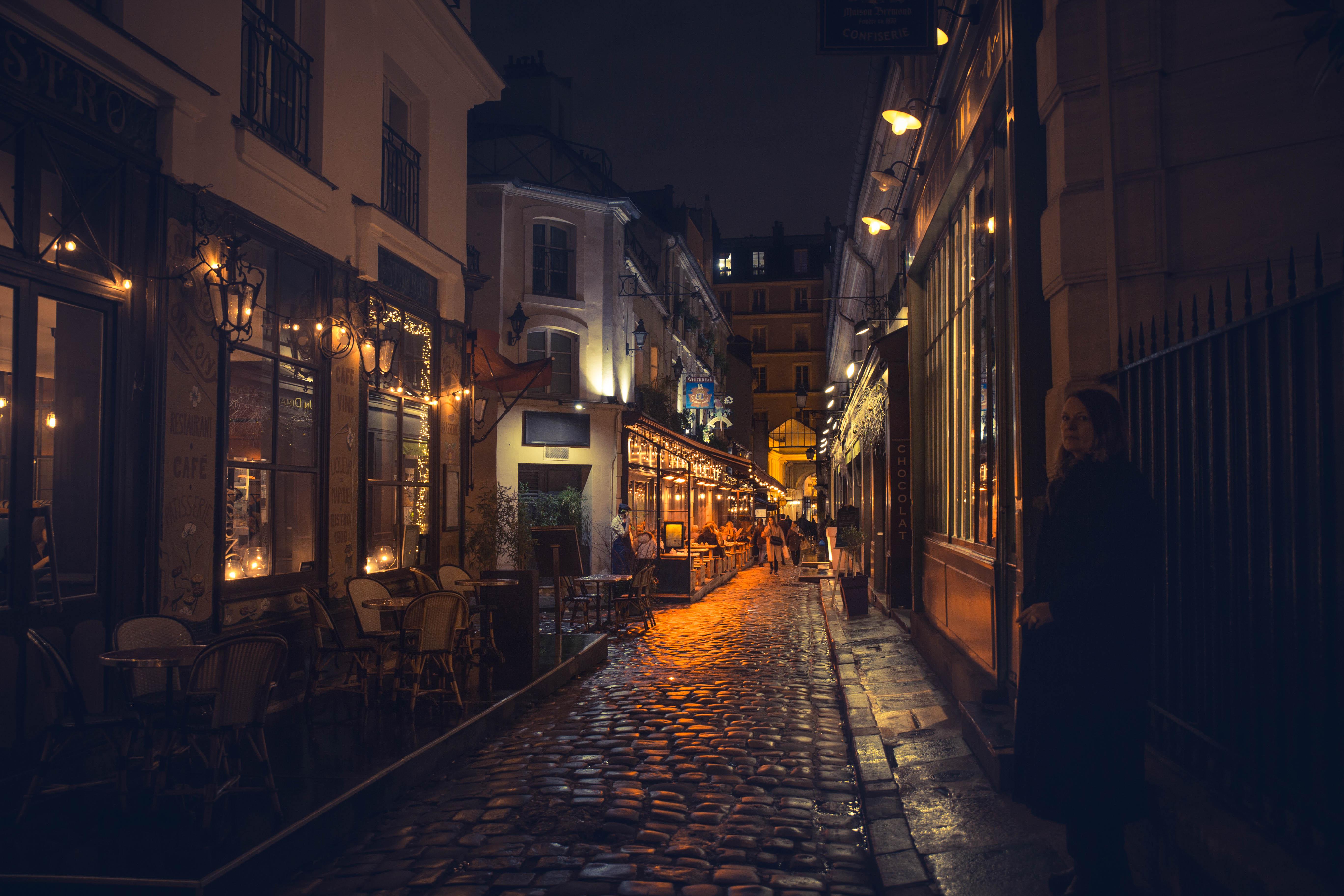 A cozy cobblestone street in a European city at night, lined with warm, inviting restaurants and shops