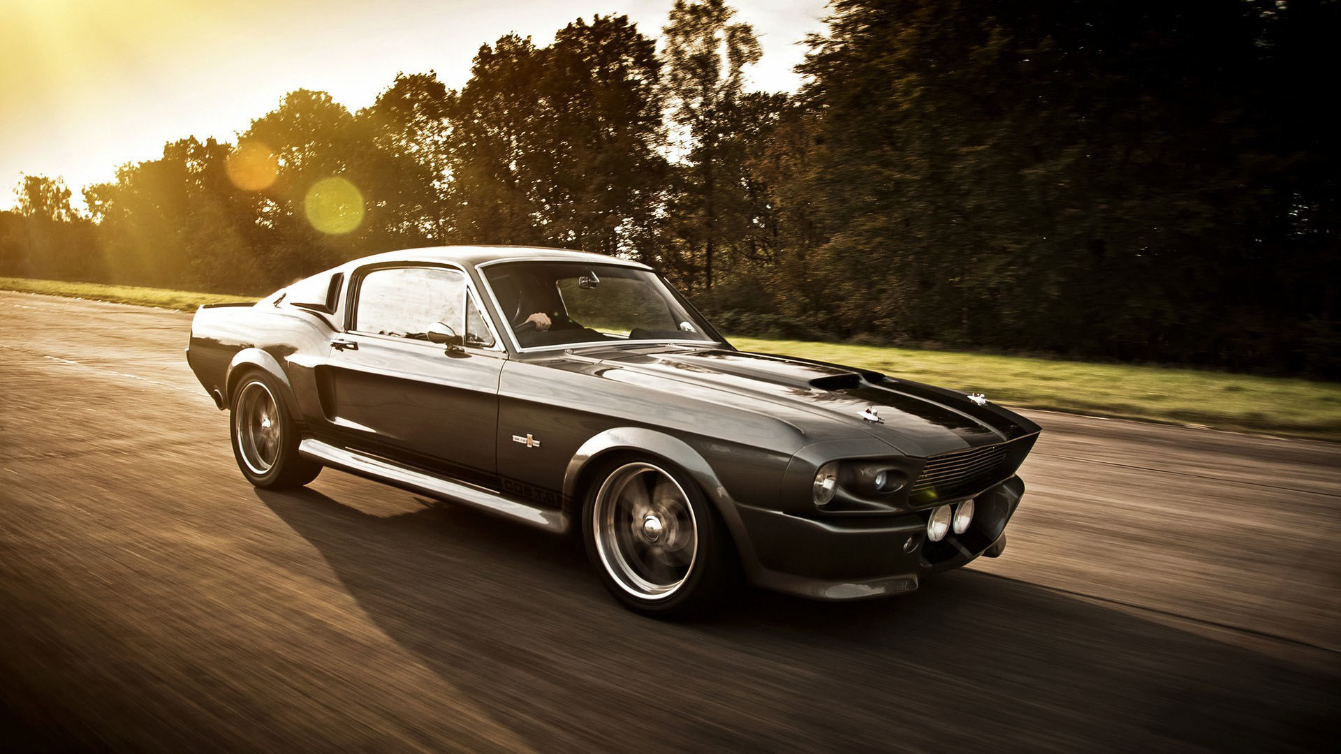 A classic Ford Mustang Shelby GT500 speeding down a road at sunset