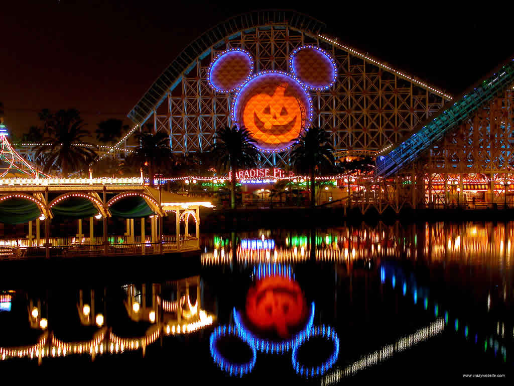 Disneyland's California Adventure park decorated for Halloween at night, featuring a giant Mickey Mouse pumpkin on the roller coaster and its reflection in the water