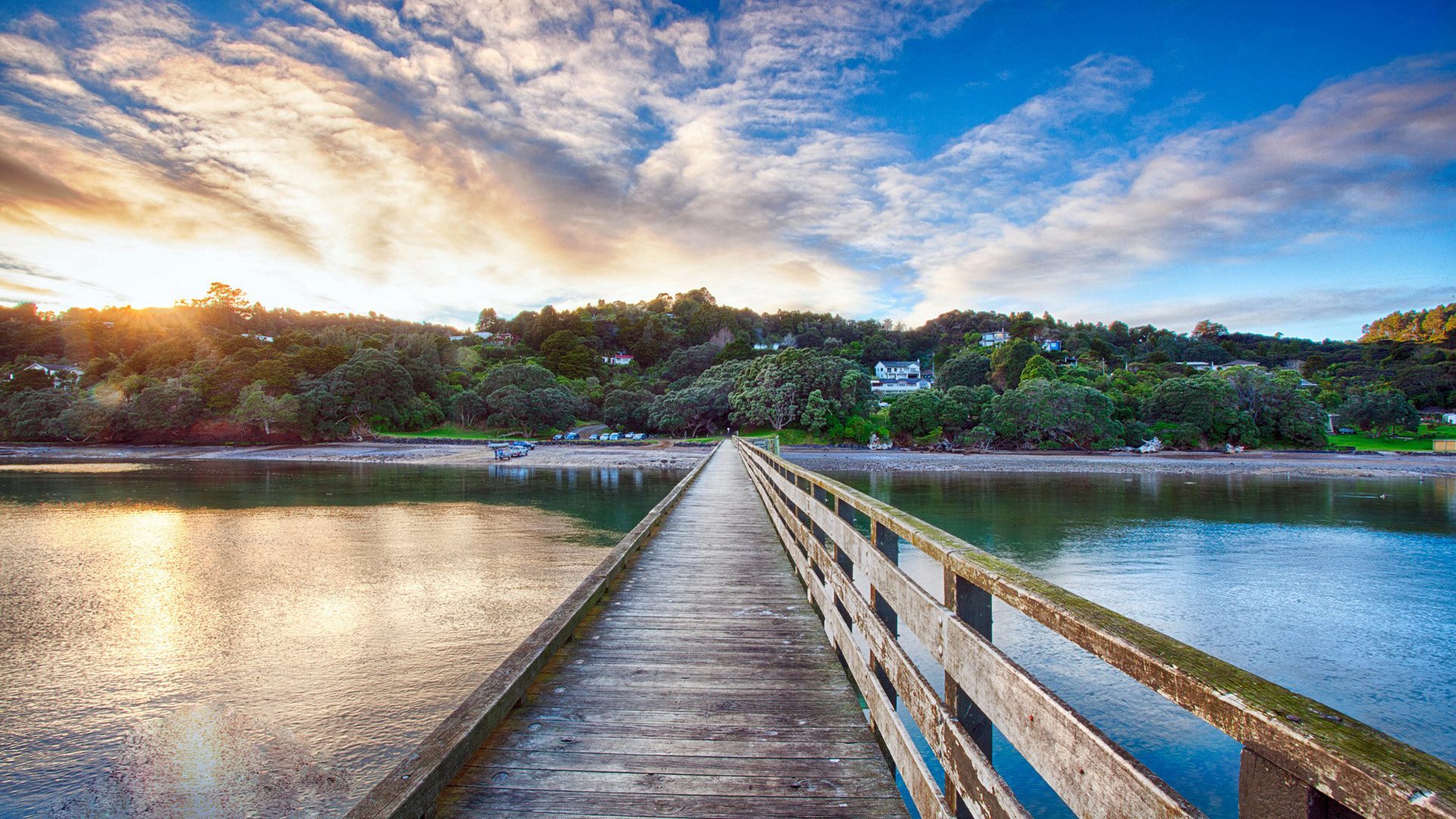 Wooden pier stretching towards a lush green shore under a vibrant sunset sky