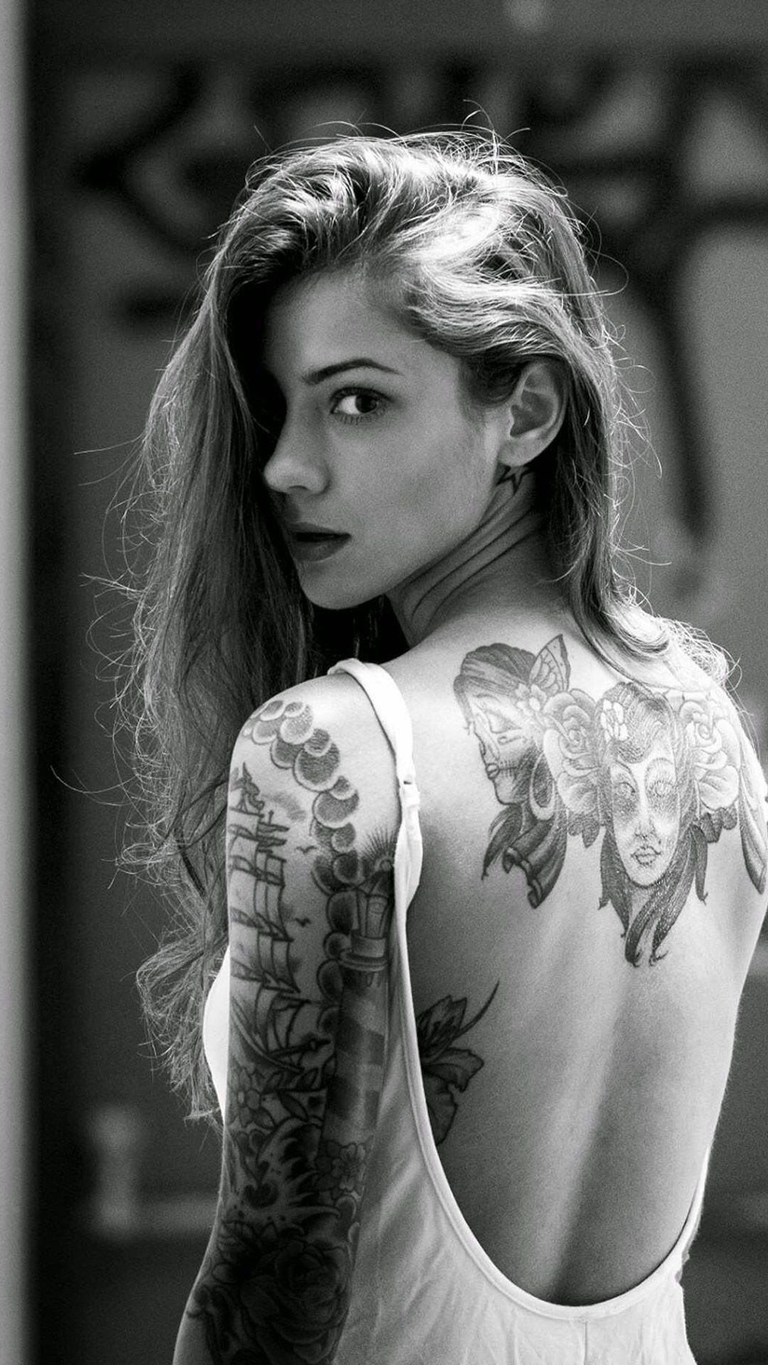 Black and white photo of a woman with intricate tattoos on her back and arm