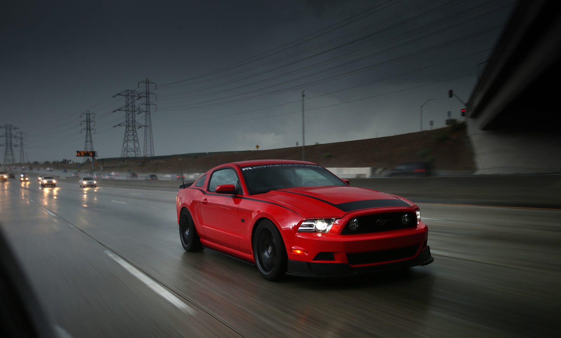 Red Ford Mustang driving on a highway in the rain