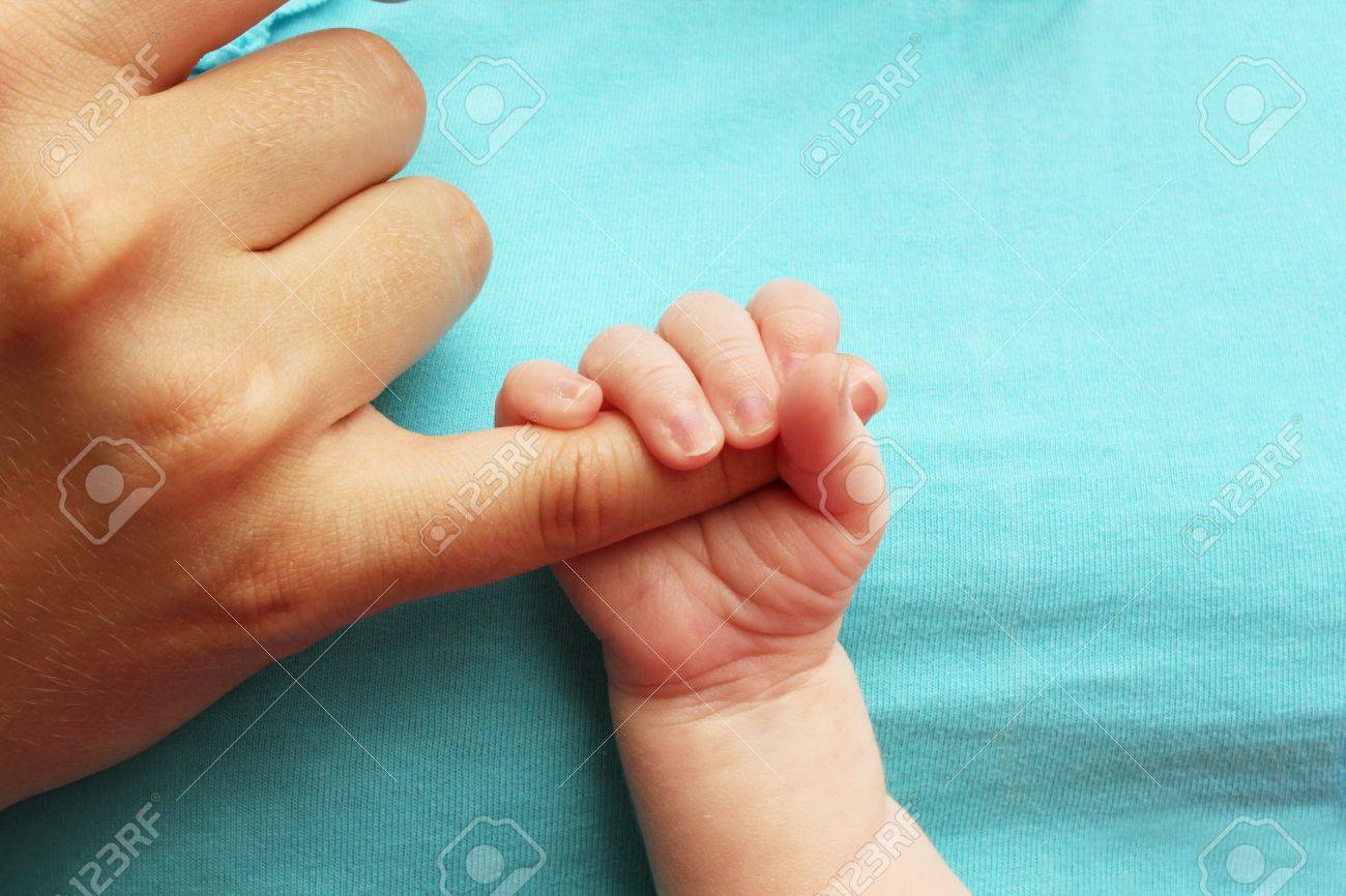 Small Baby Holding Parents Hand On Blue Background Stock Photo