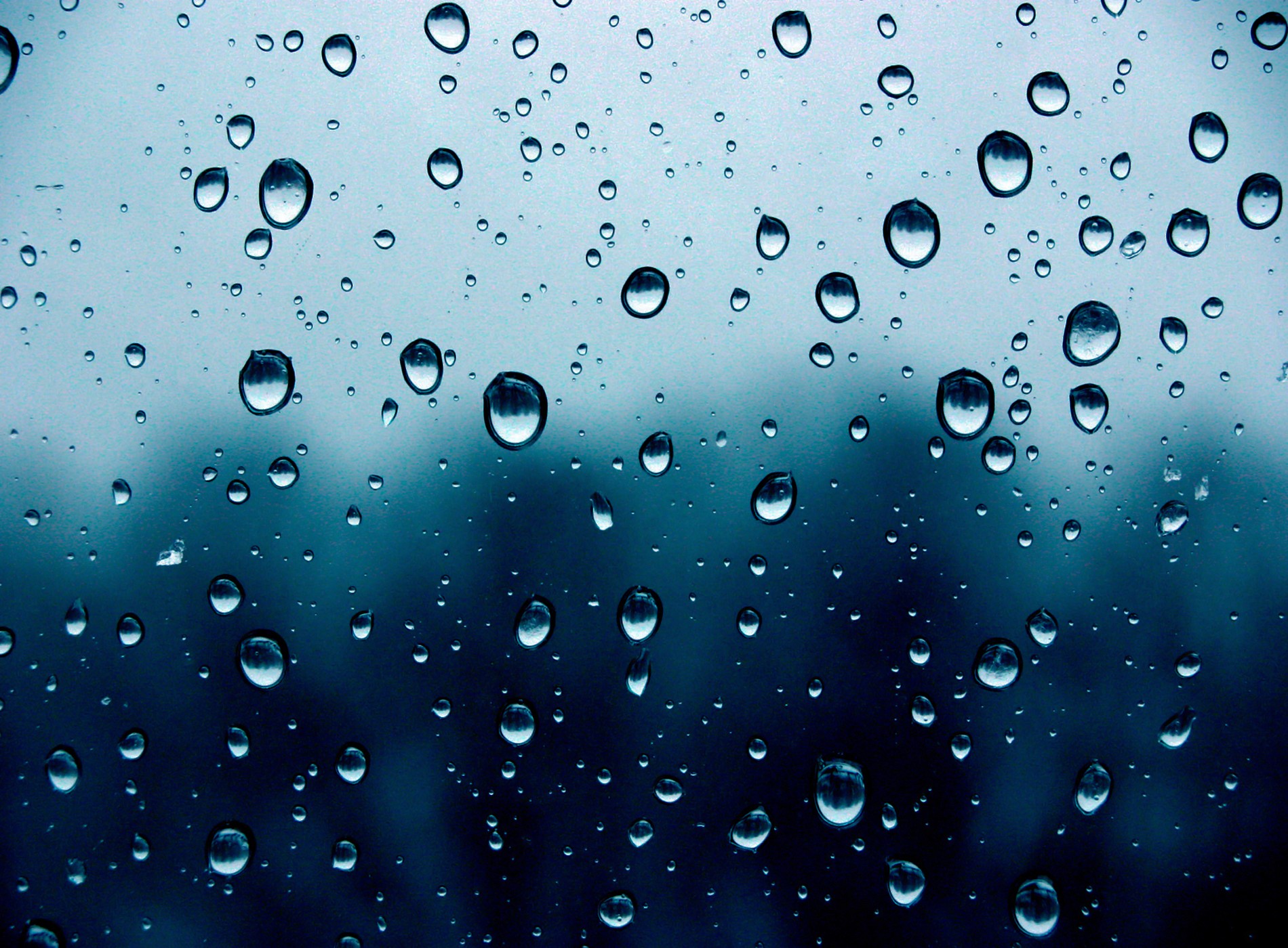 Close-up of raindrops on a window pane with a blurred dark blue background