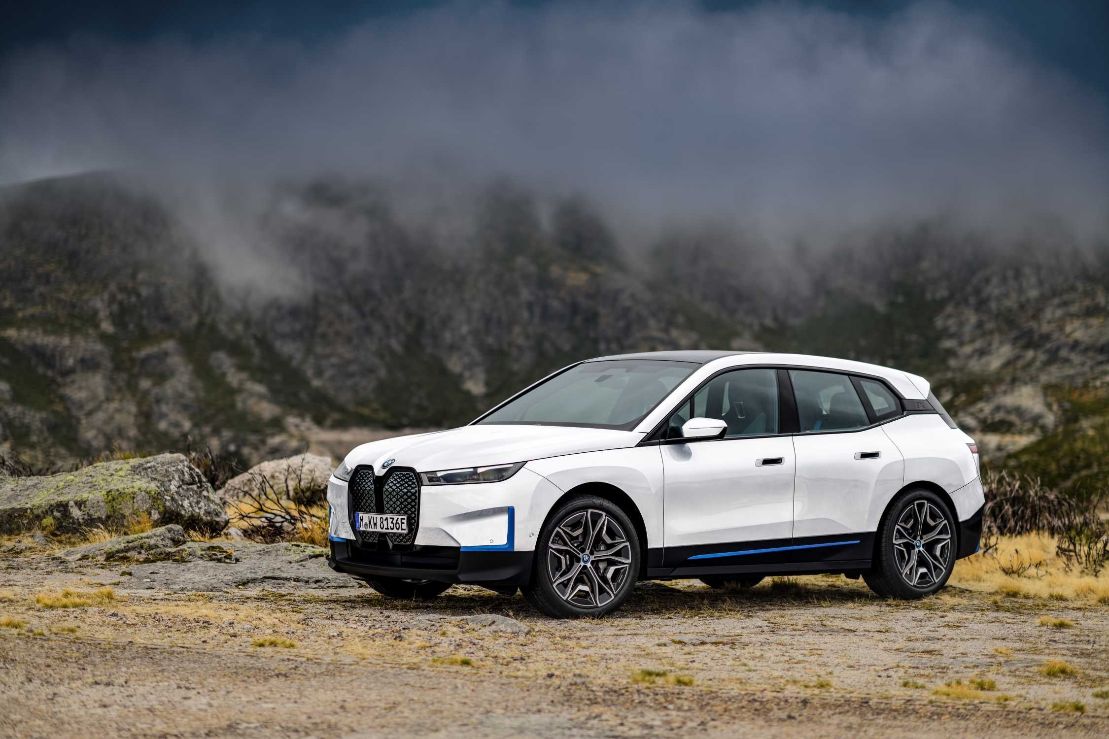 A white BMW iX electric SUV parked on a mountain road with a foggy, mountainous backdrop