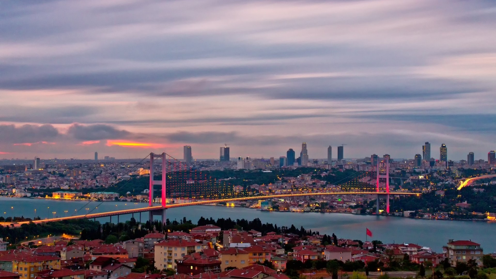 A stunning panoramic view of Istanbul at sunset, featuring the Bosphorus Bridge illuminated against the vibrant cityscape