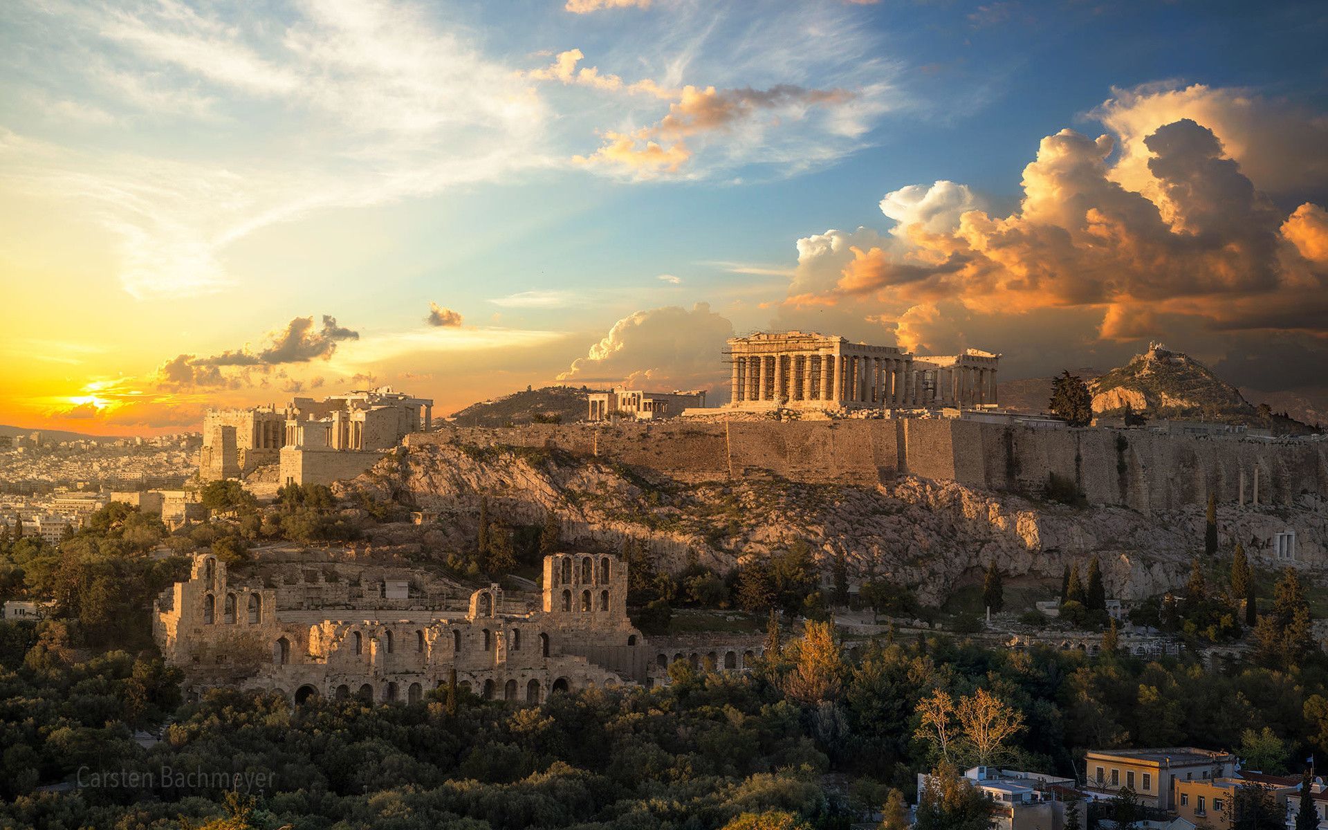 A breathtaking sunset panorama of the Acropolis in Athens, Greece, showcasing the Parthenon and other ancient ruins against a backdrop of vibrant clouds and the cityscape