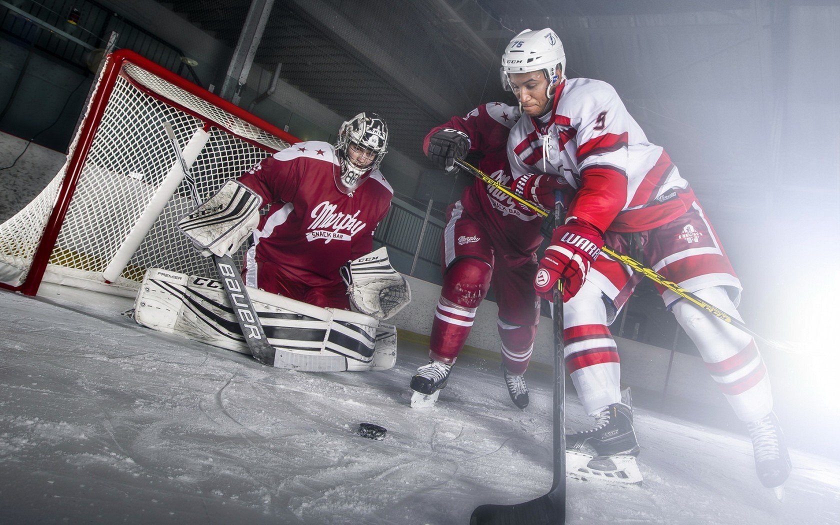 Action shot of an ice hockey player taking a shot on goal, with the goalie defending the net