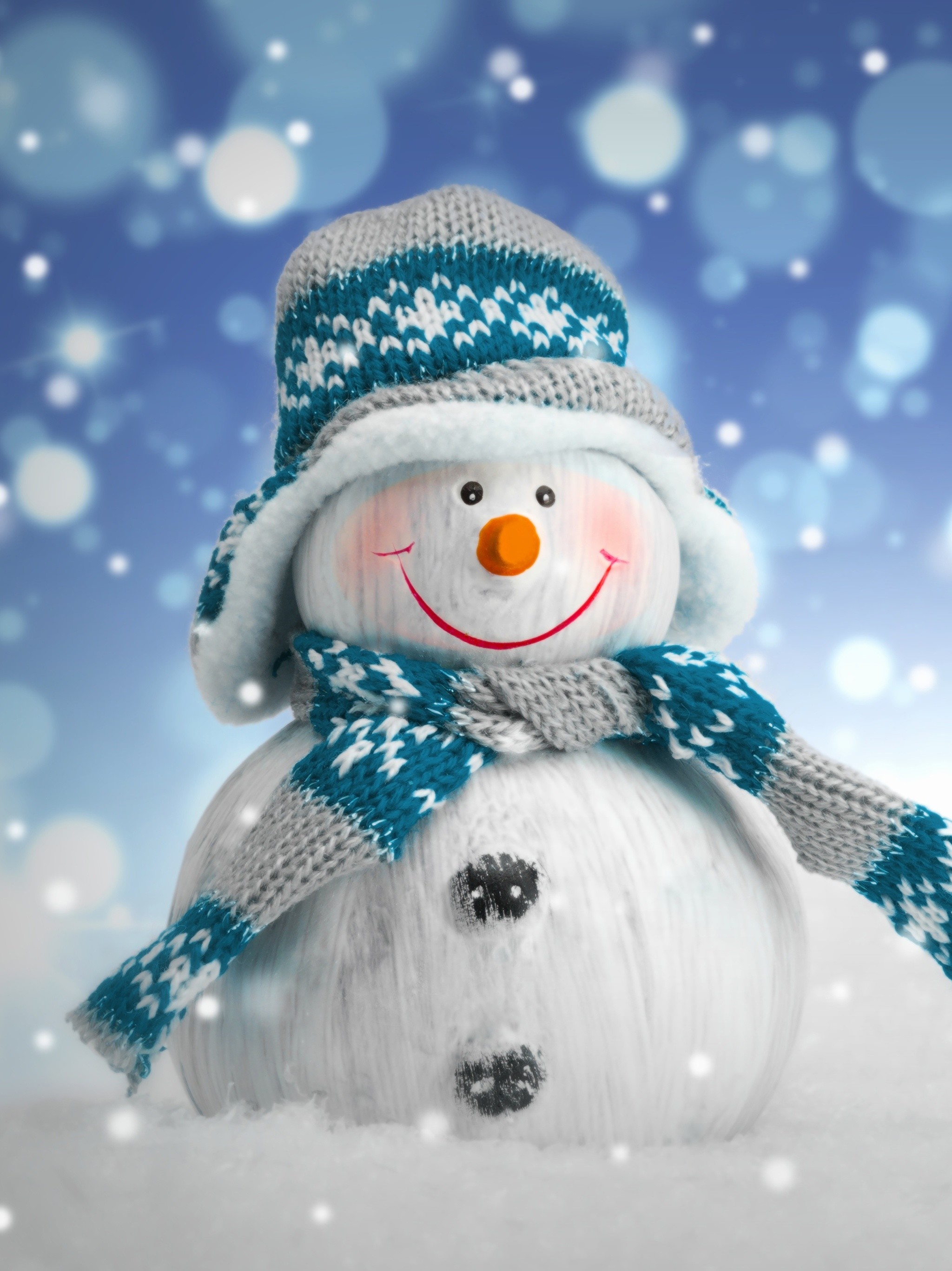 A cheerful knitted snowman stands in the snow against a backdrop of festive bokeh lights