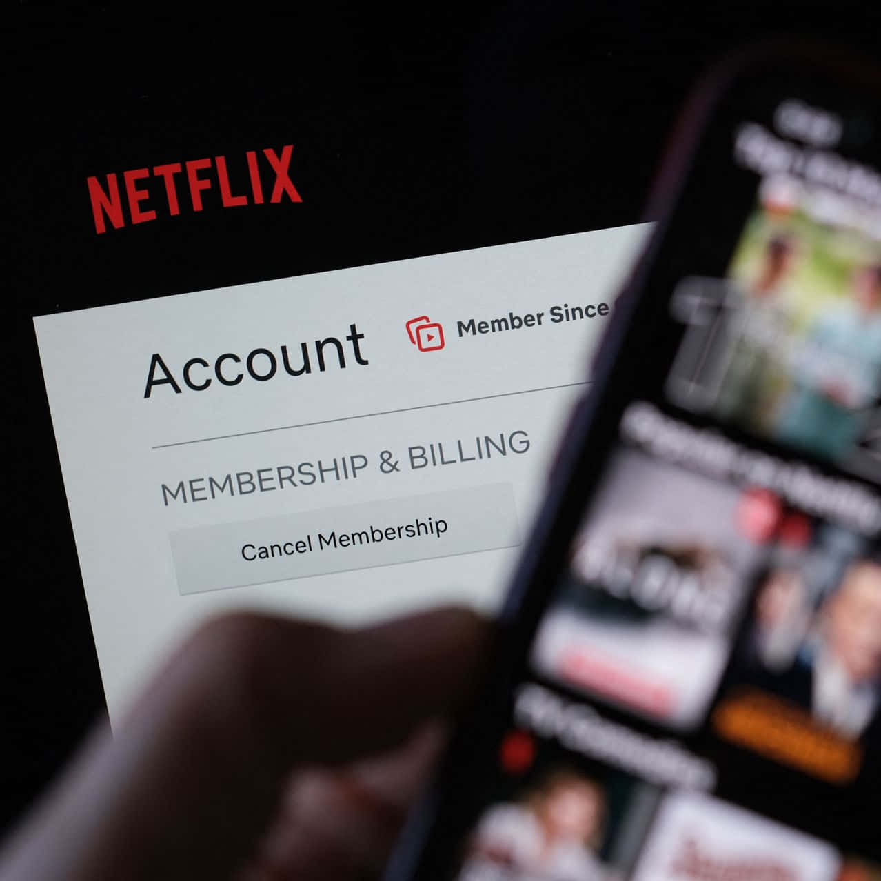 A close-up view of a Netflix account page on a digital device, with the 'Cancel Membership' button highlighted.  A blurred phone screen displaying Netflix content is superimposed