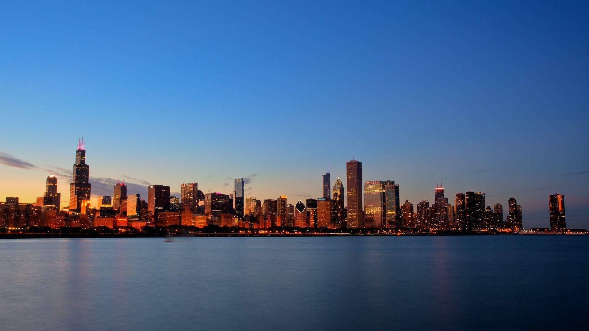 Chicago skyline at dusk with skyscrapers lit up and reflecting in the calm waters of Lake Michigan