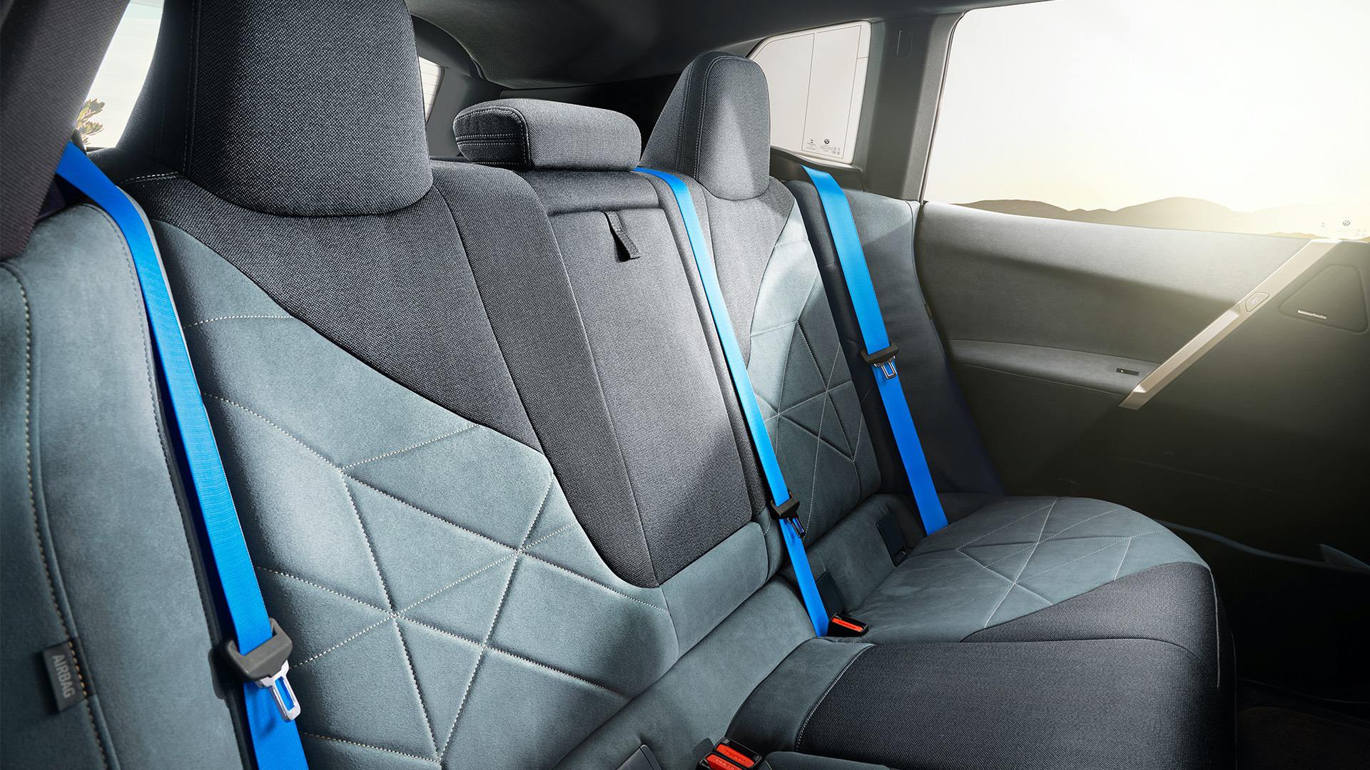 Close-up view of the back seats of a BMW iX, showcasing the unique geometric pattern of the upholstery and the bright blue seatbelts
