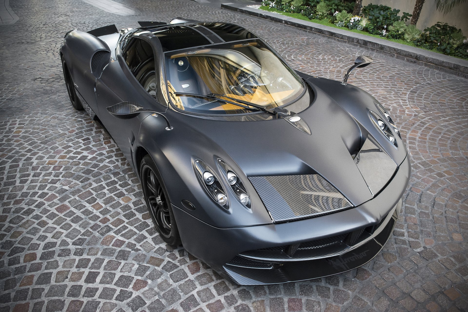 A sleek, dark gray Pagani Huayra parked on a cobblestone driveway