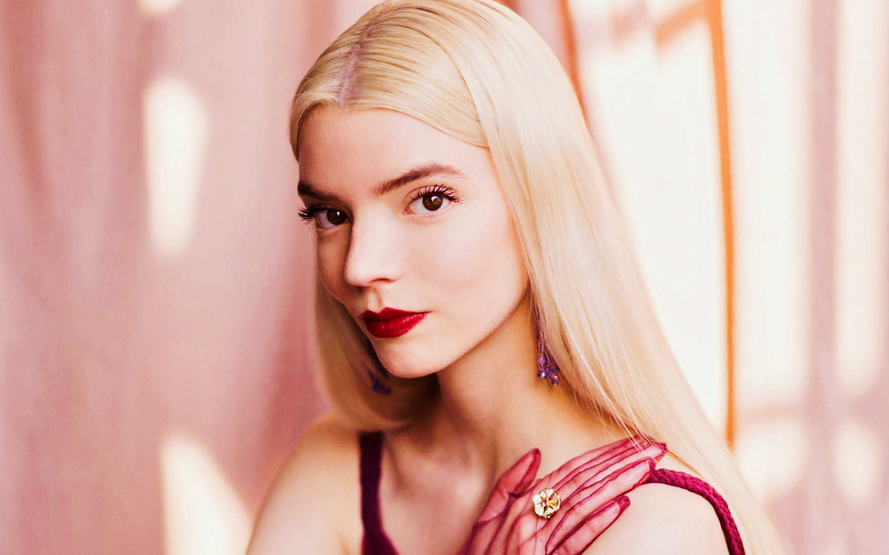 Anya Taylor-Joy poses elegantly in a burgundy dress and red gloves against a soft pink backdrop