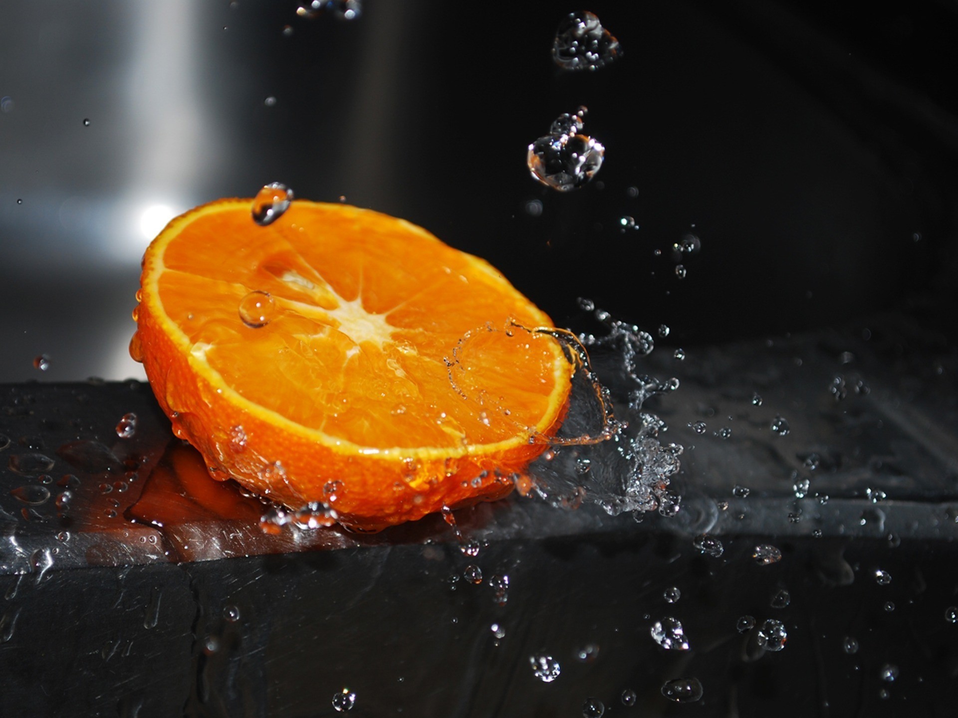 A juicy slice of orange with water droplets splashing around it