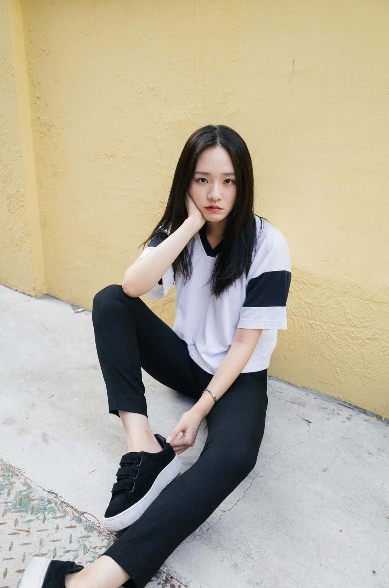 A Young Woman Sitting On The Ground Wearing Black Pants And White T Wallpaper