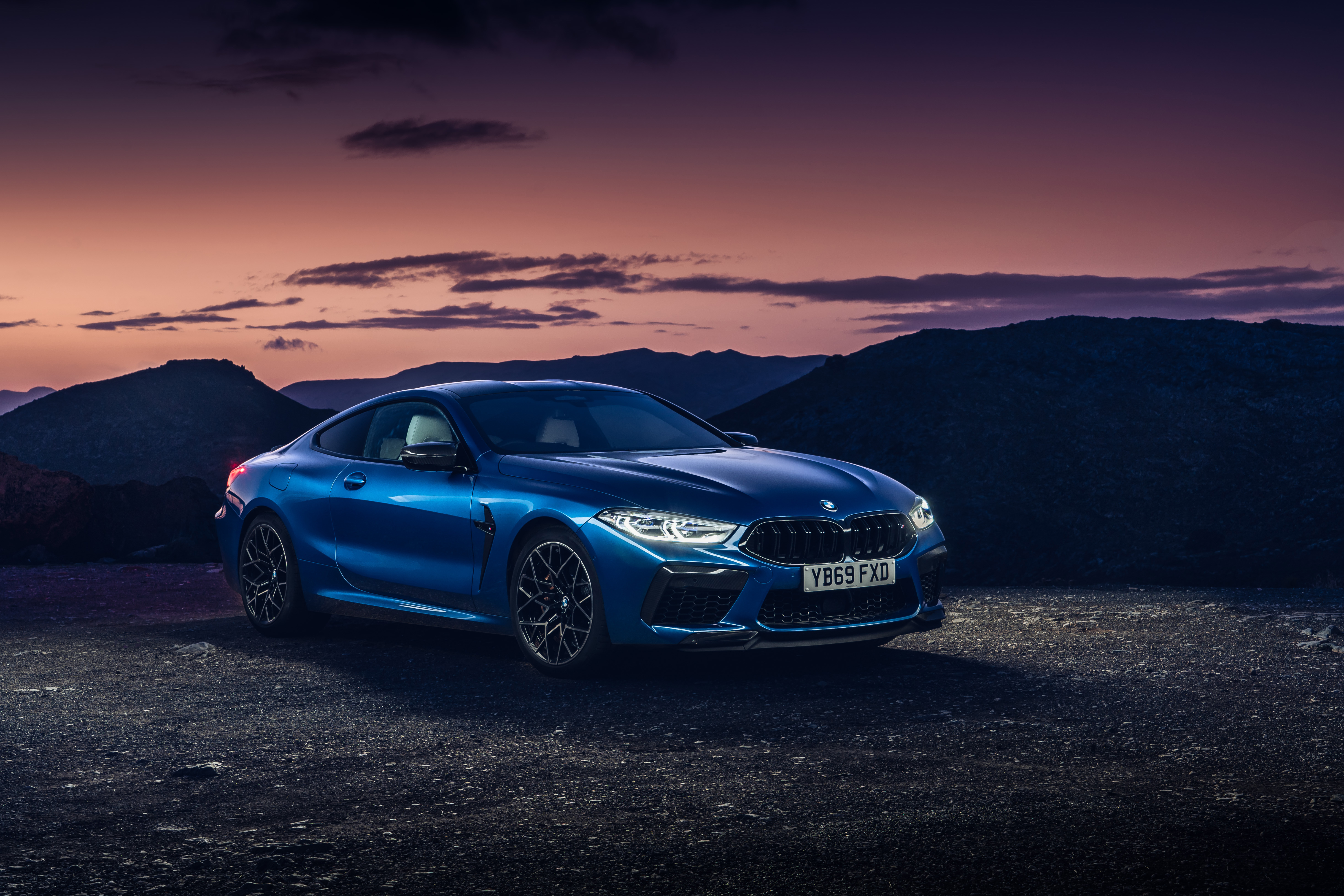 A blue BMW M8 Competition Coupe parked against a stunning sunset backdrop