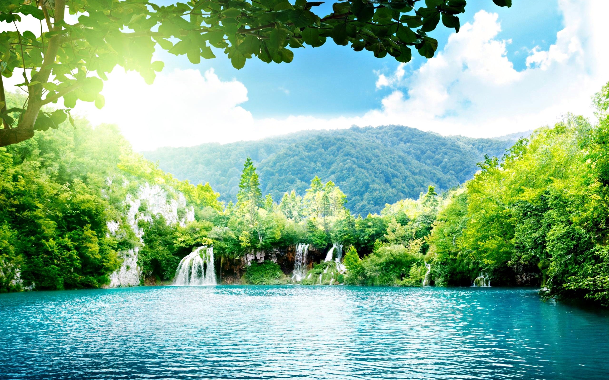 Scenic waterfall cascading into a turquoise lake surrounded by lush green forest, perfect for a computer wallpaper